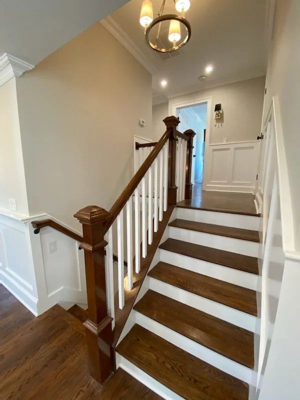 Staircase with wood railings, white walls, and carpeted steps in a bright hallway