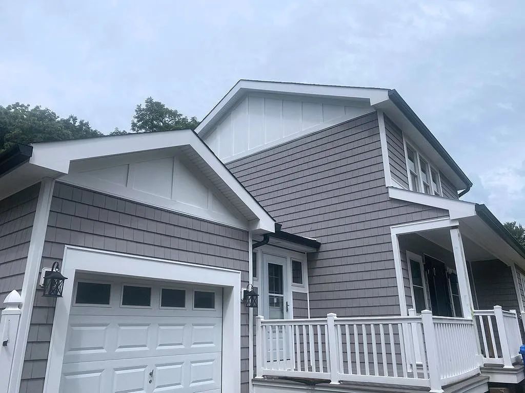 Gray house with garage and white porch railings under a cloudy sky