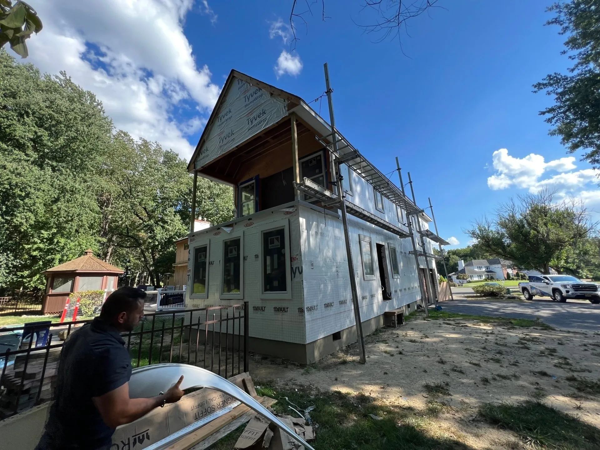 Old white two-story house with a porch, under renovation, beside a seated person outdoors.