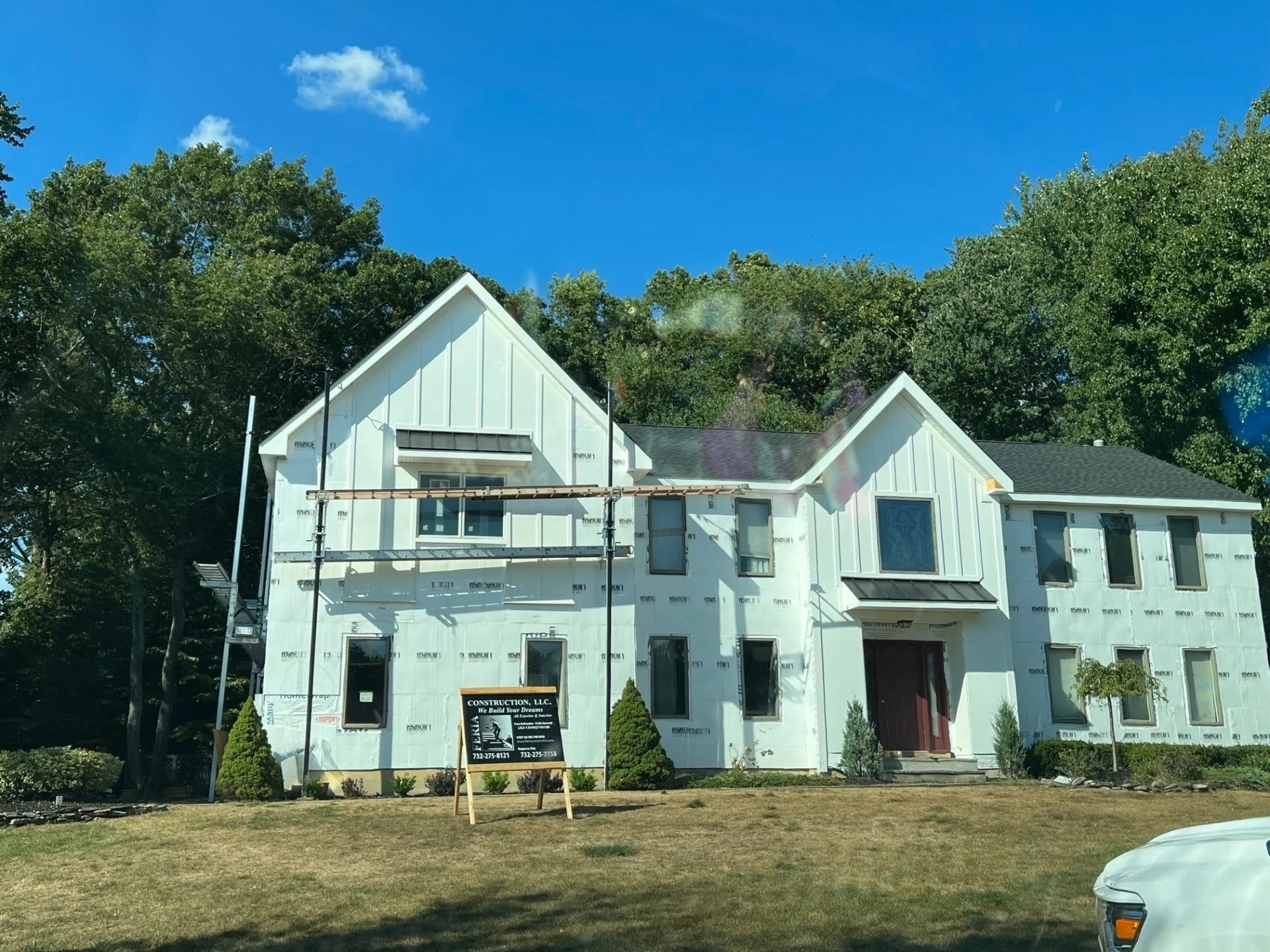 White two-story house with a front porch and sign, surrounded by trees under a bright blue sky