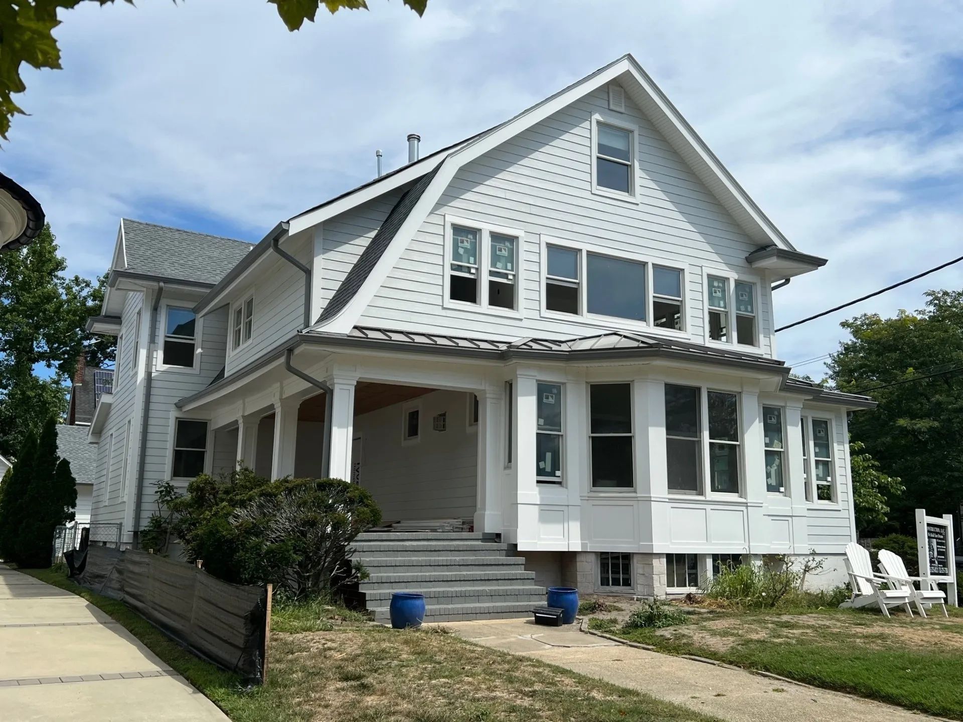 White two-story house with wraparound porch and gabled roof on a sunny street