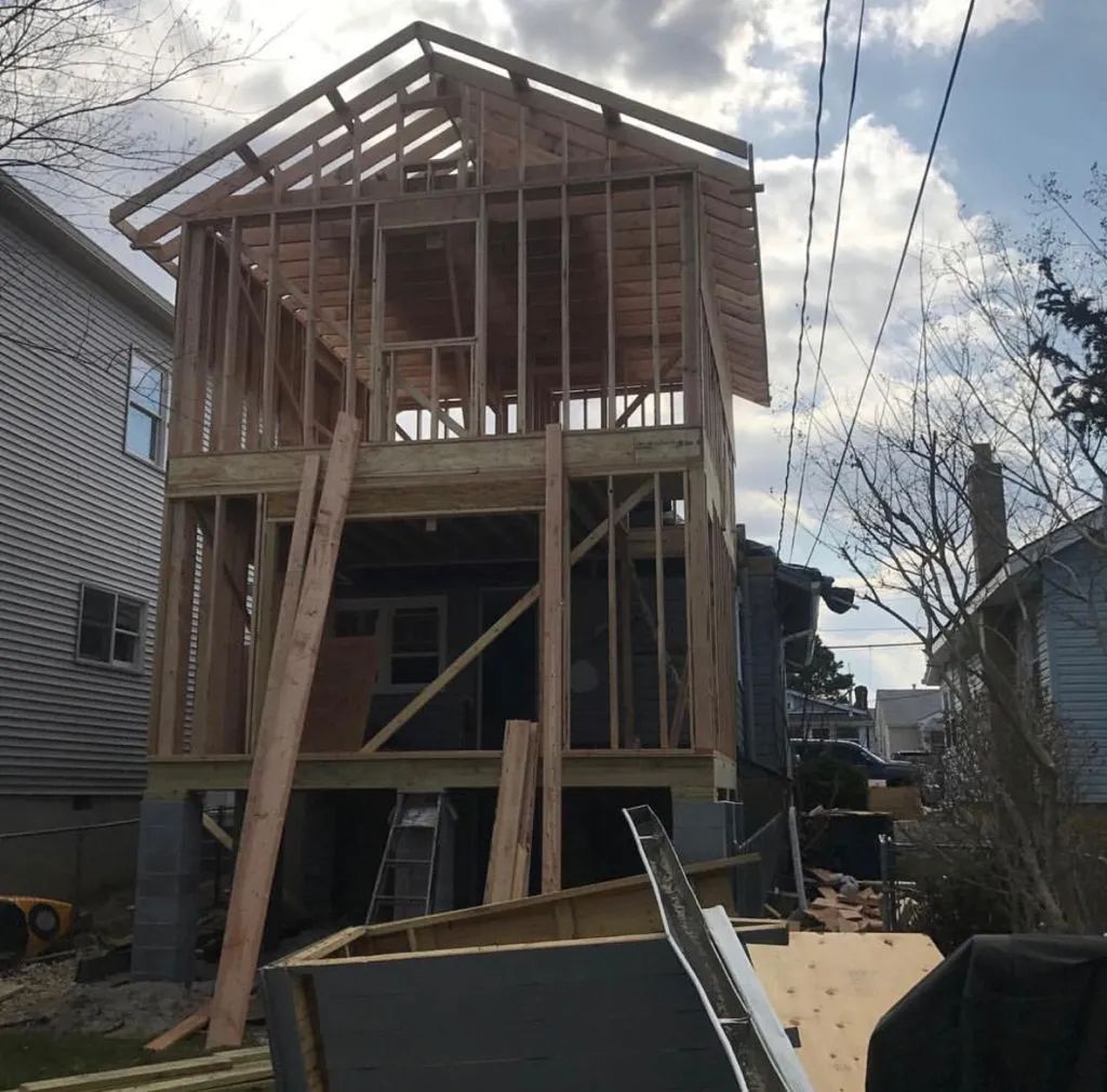 Partially framed two-story house under construction with exposed wooden beams and cloudy sky