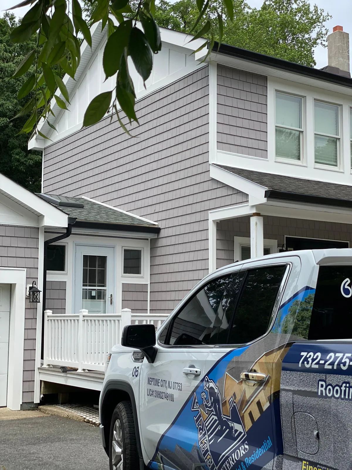 Gray two-story house with white trim and a roofing company truck parked in front