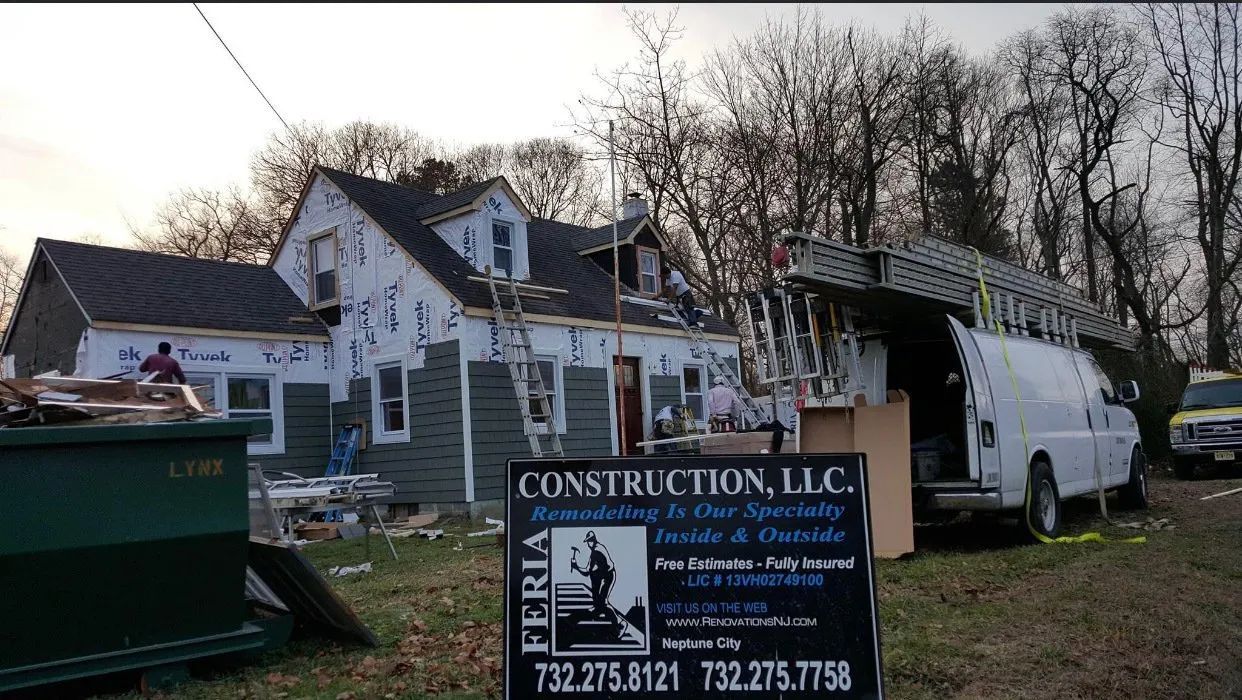 Construction site with blue house, white work truck, dumpster, and sign in front of trees at dusk