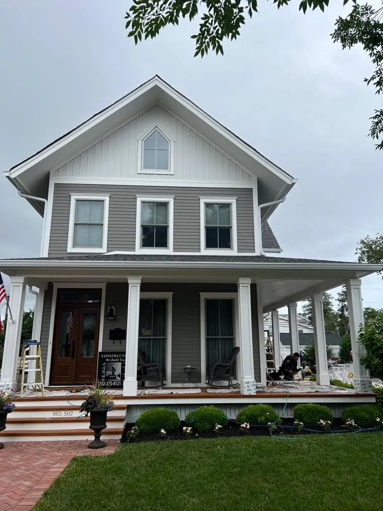 Gray two-story house with white trim, front porch, and brick steps beside a green lawn