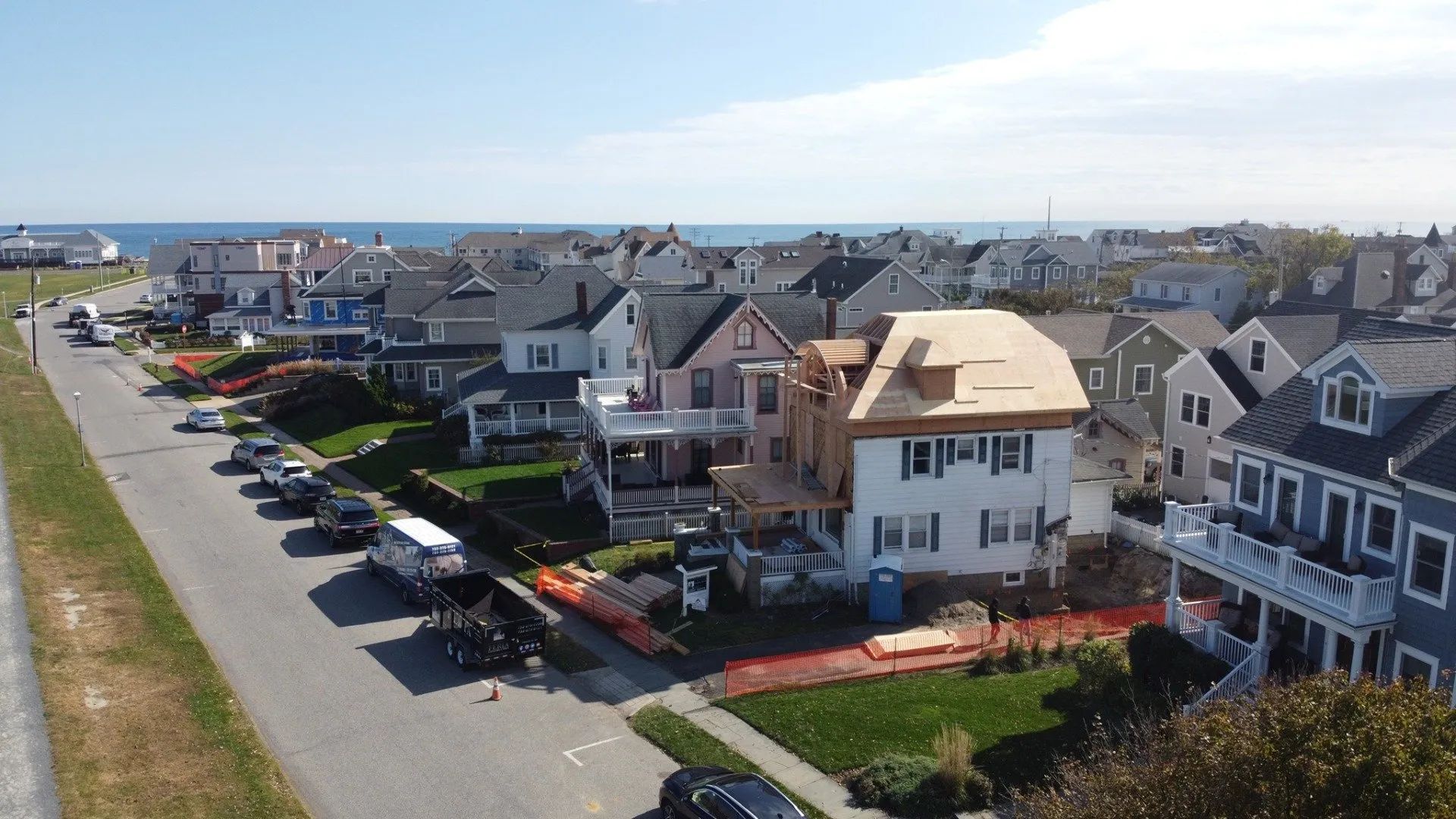 Aerial view of a seaside neighborhood with rows of houses beside a waterfront road.