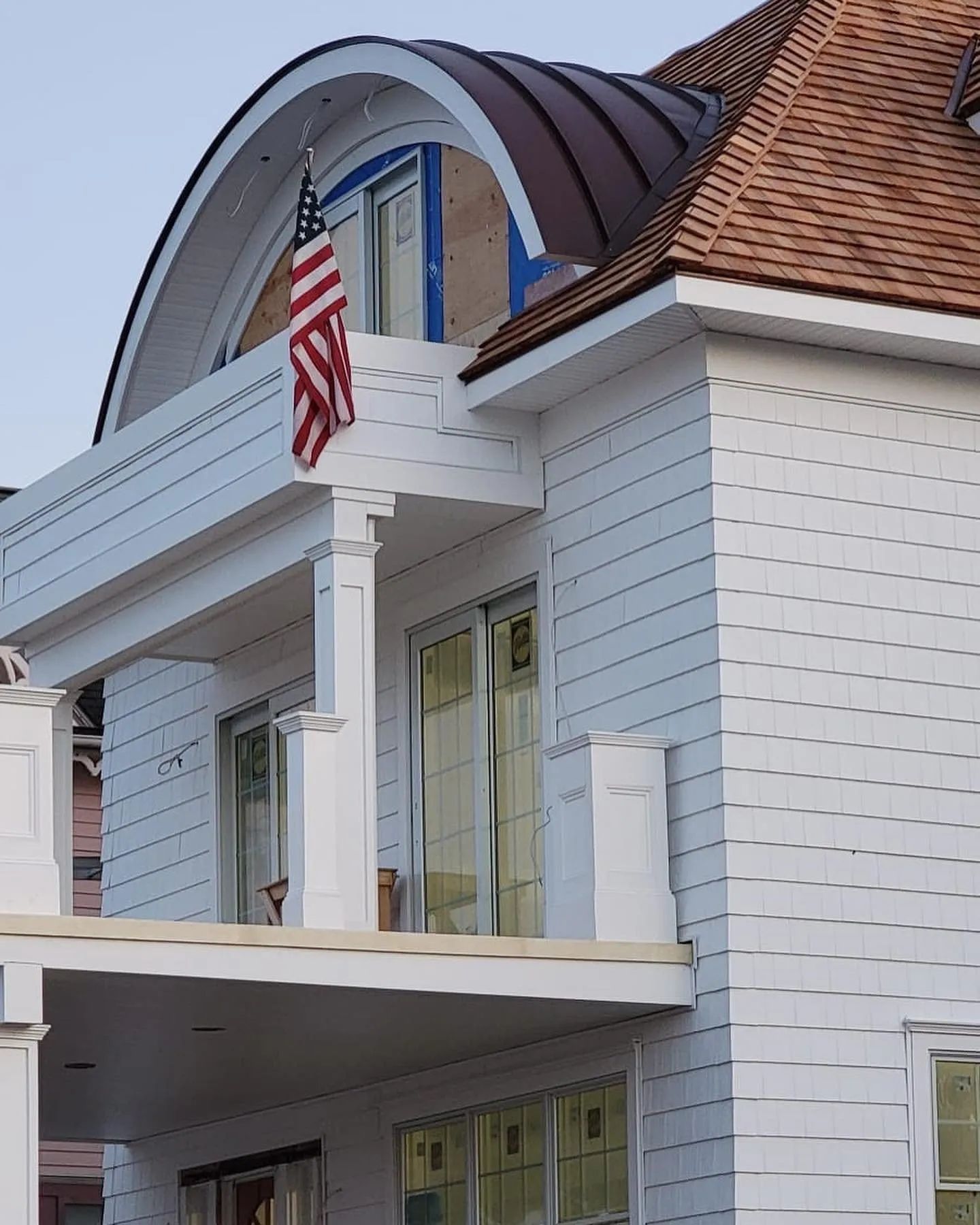 White house with porch columns, red shingled roof, and an American flag hanging by the entrance