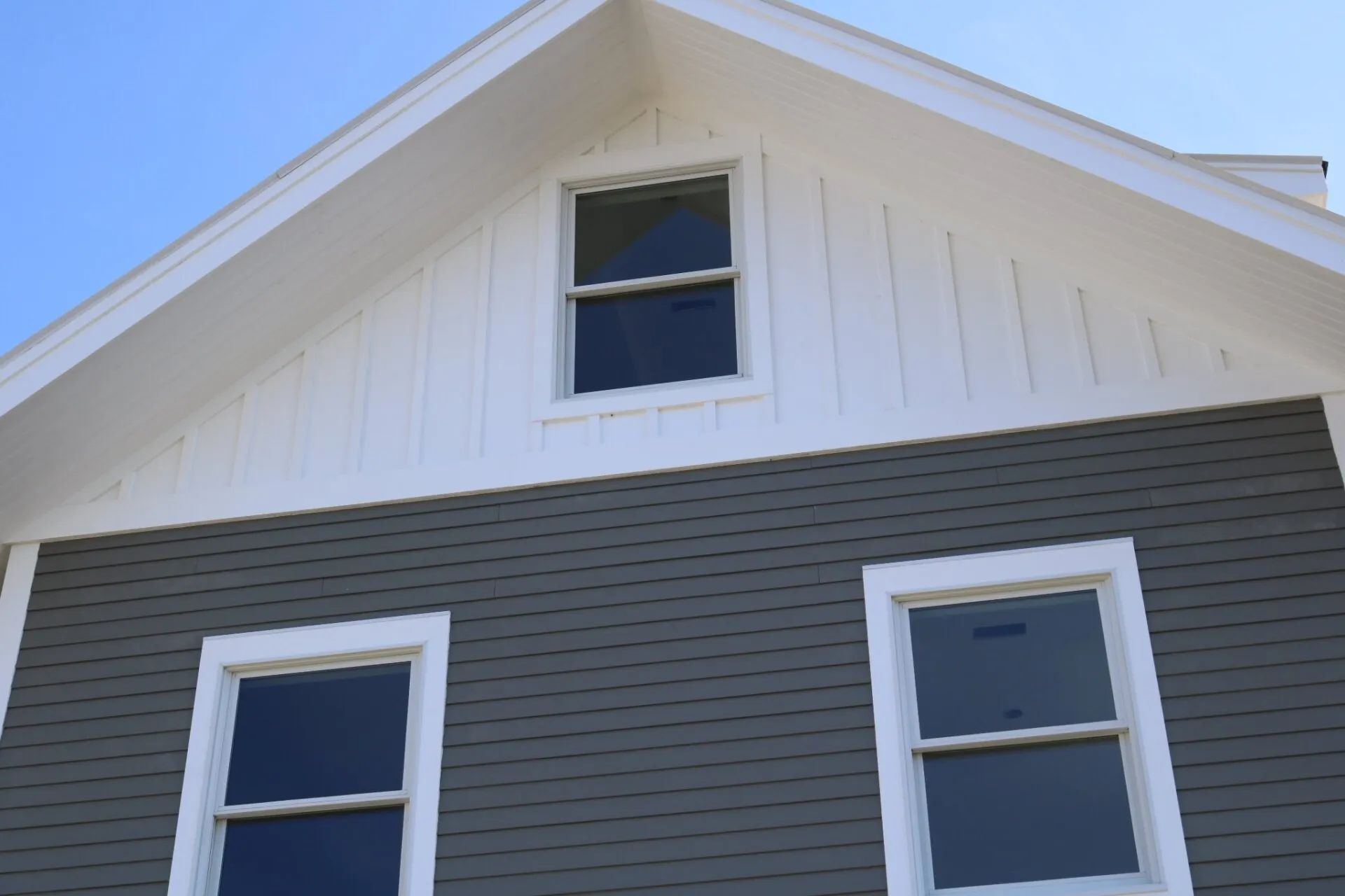 White and gray house gable with three windows against a blue sky
