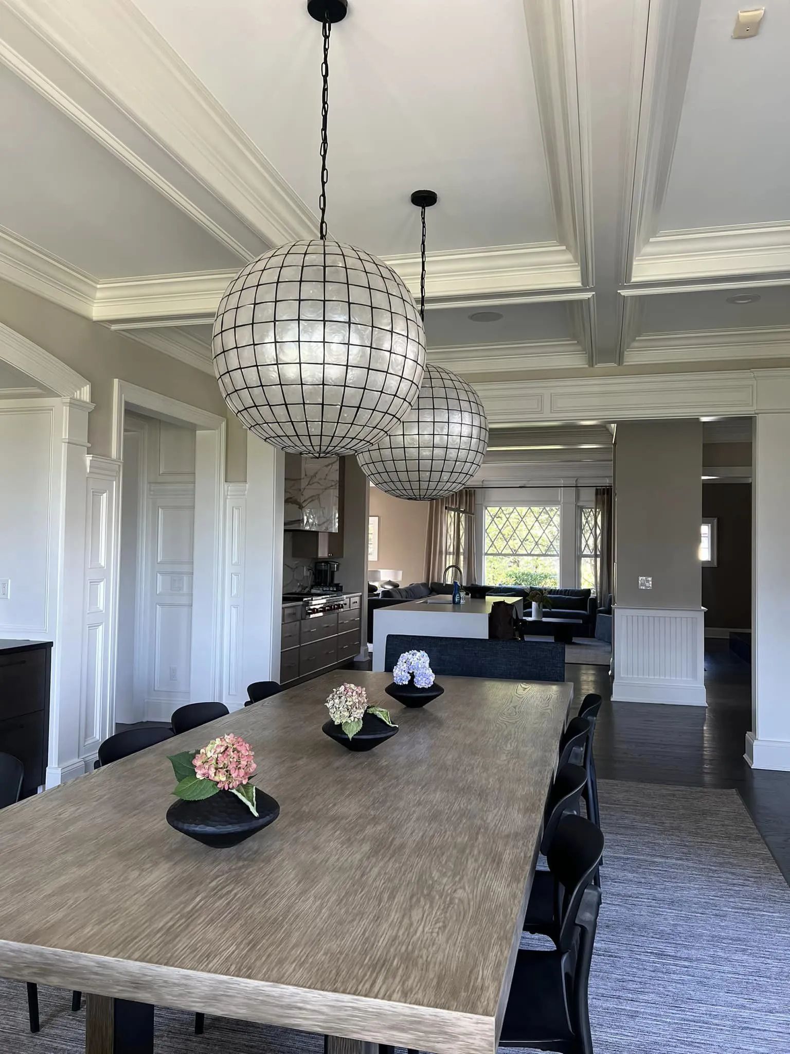 Elegant dining room with long table, black chairs, and modern pendant lights under a coffered ceiling