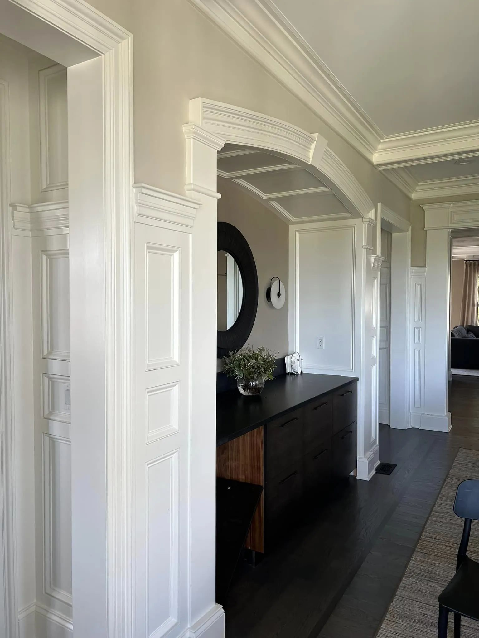 White hallway with ornate trim, arched doorway, dark console table, and mirror in a bright interior.