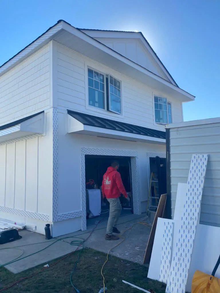 Person carrying items into an open garage beside a white house on a clear day