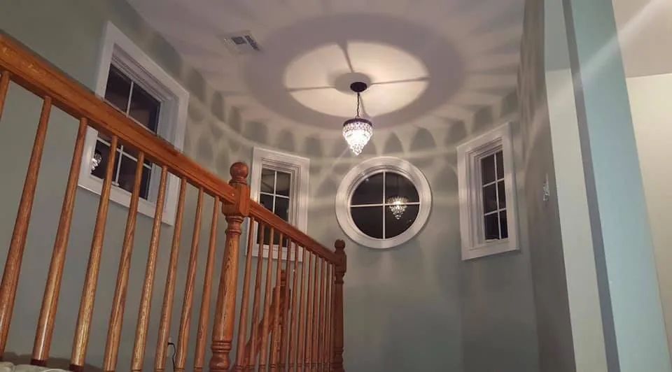 Stairwell landing with wooden railing, round window, hanging light, and circular shadow pattern on the ceiling