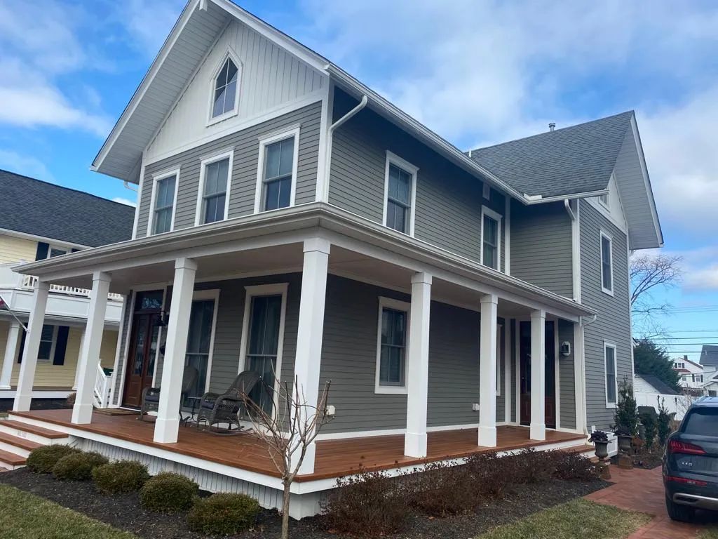 Two-story gray house with white trim and a wraparound porch on a residential street