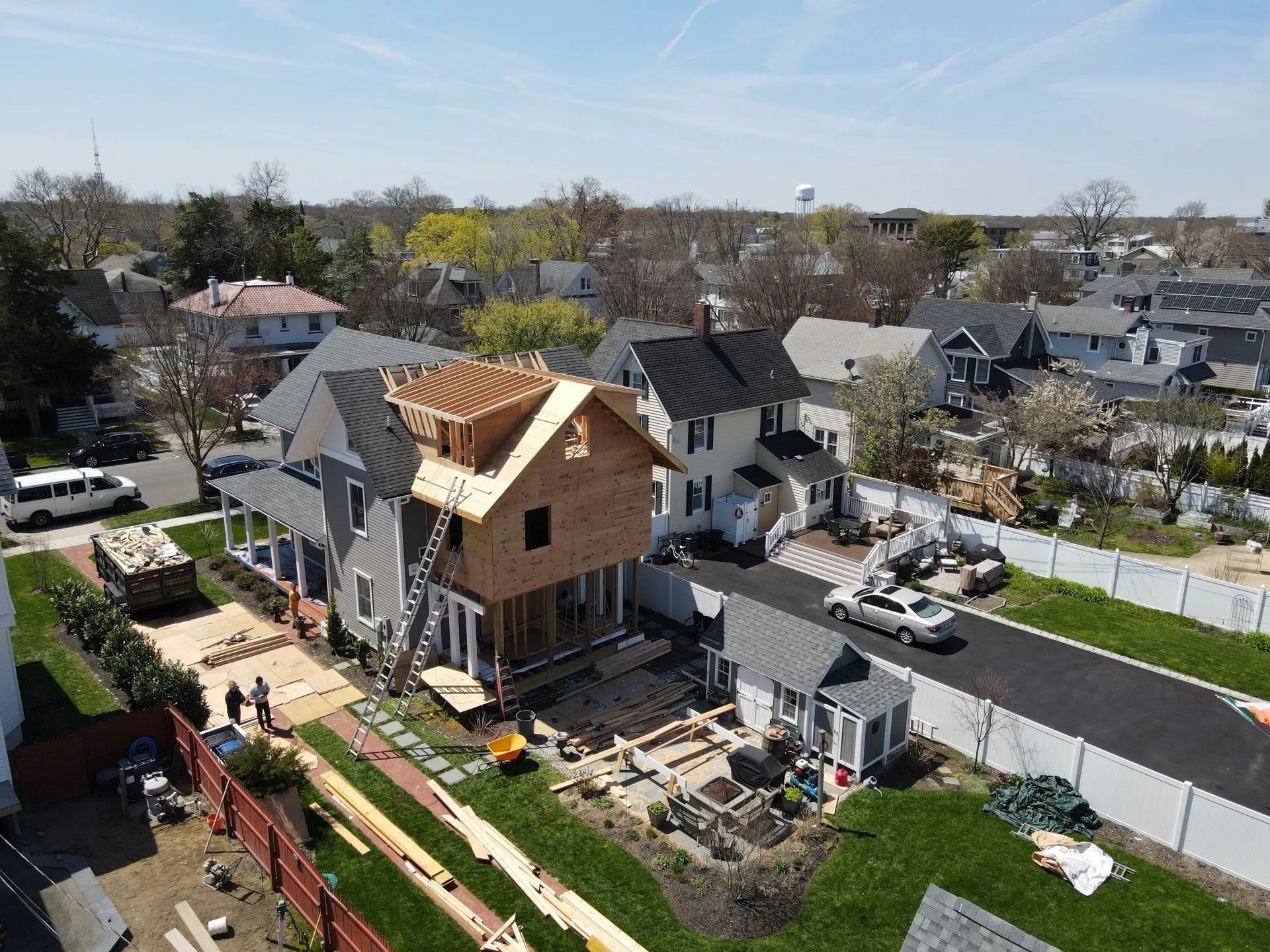 Aerial view of a house under construction in a suburban neighborhood, with framing, roof sheathing, and yard work.