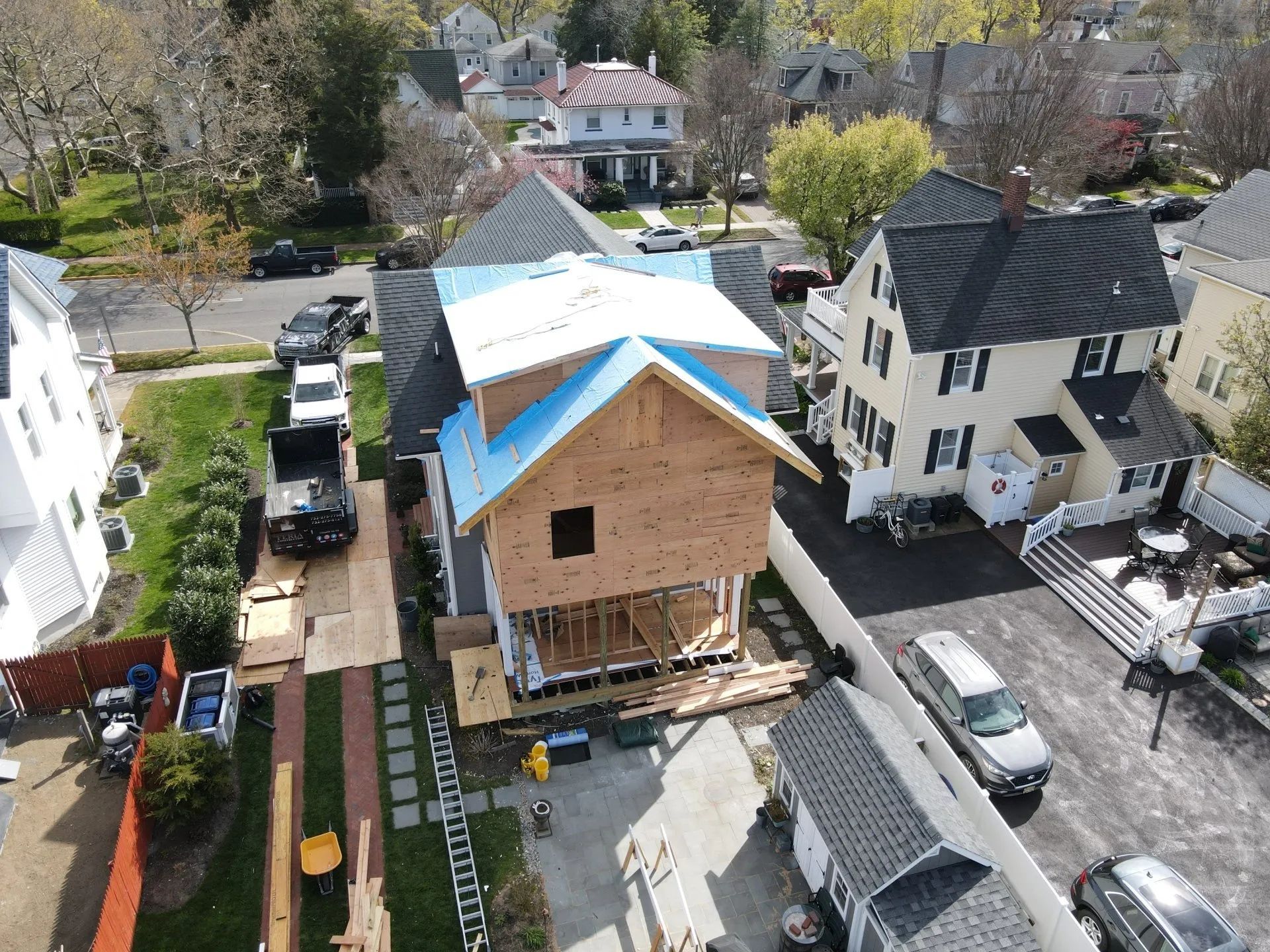 House under construction with blue roof tarp in a suburban neighborhood, viewed from above.