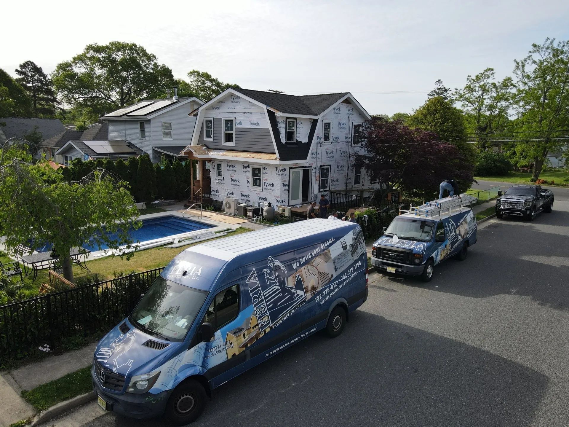 Blue service vans parked on a residential street beside a house with a pool under renovation