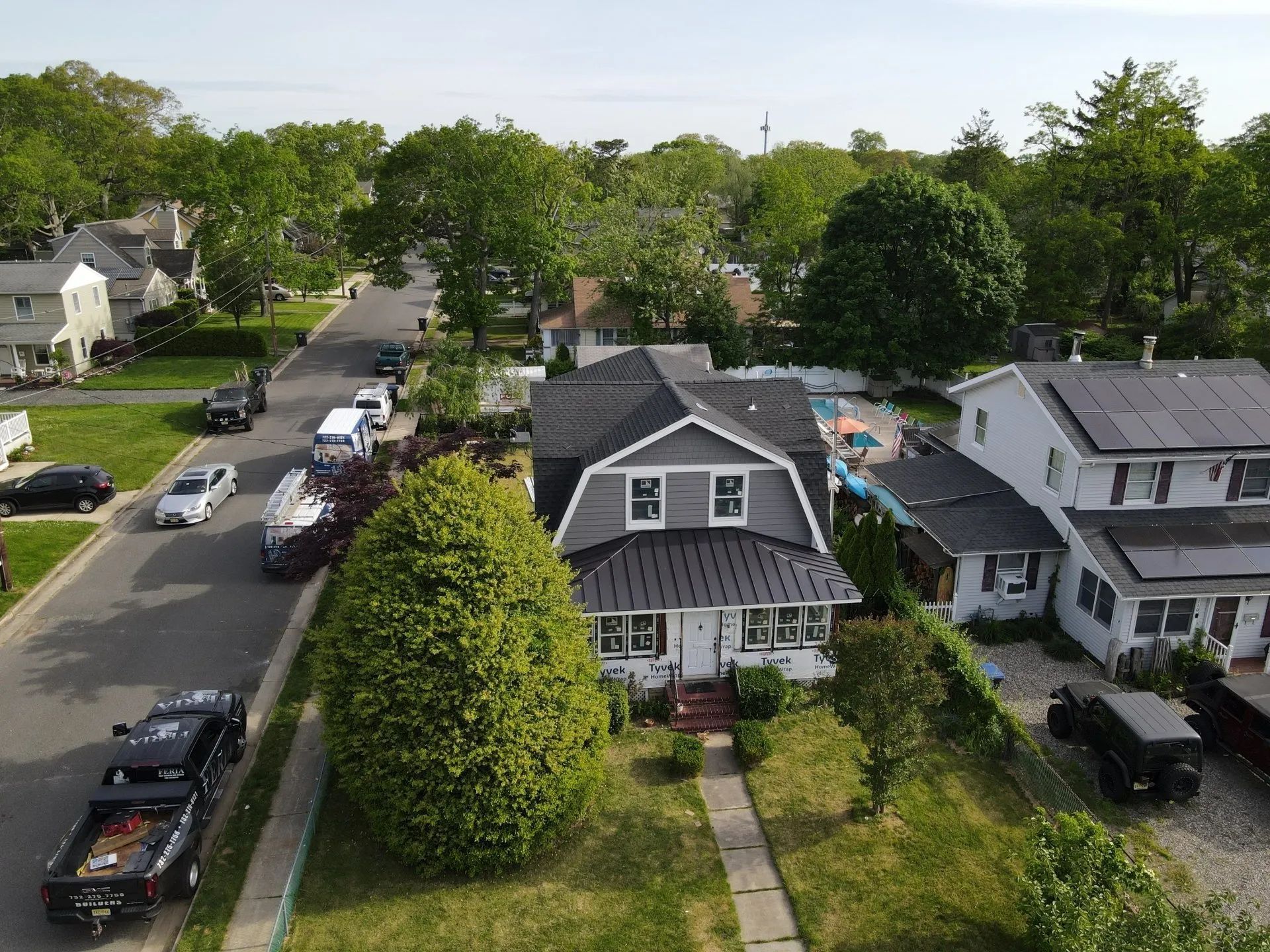 Aerial view of a suburban street with parked cars and two houses, one with a green lawn and walkway.