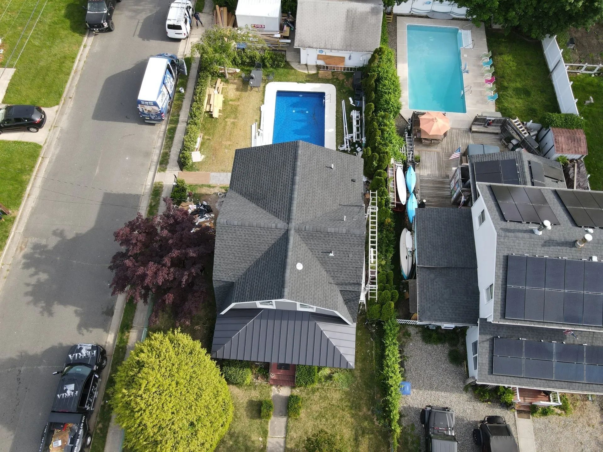 Aerial view of homes with swimming pools, parked cars, and a residential street