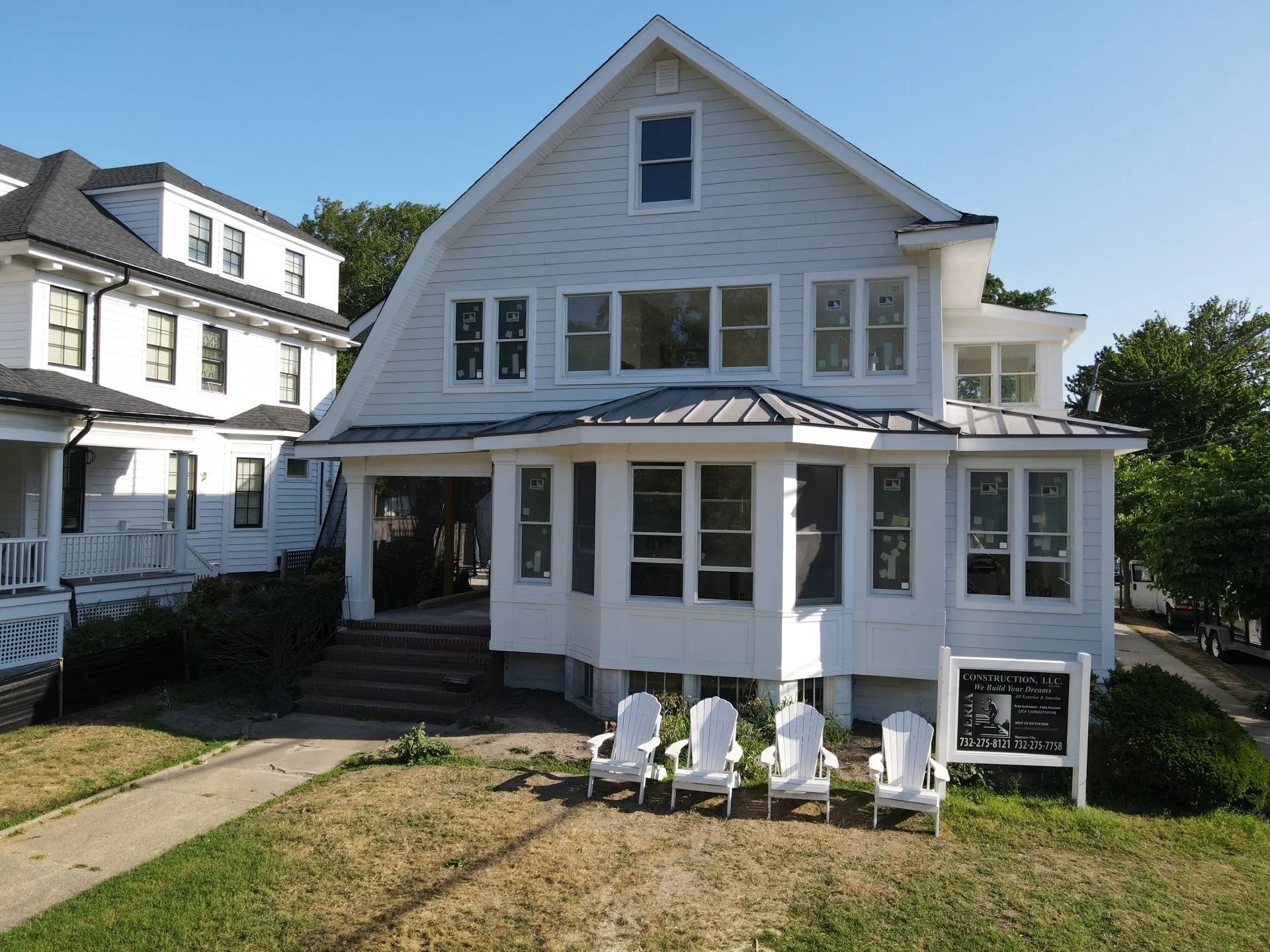 White house with porch and stairs, front lawn with four white chairs under a bright blue sky.