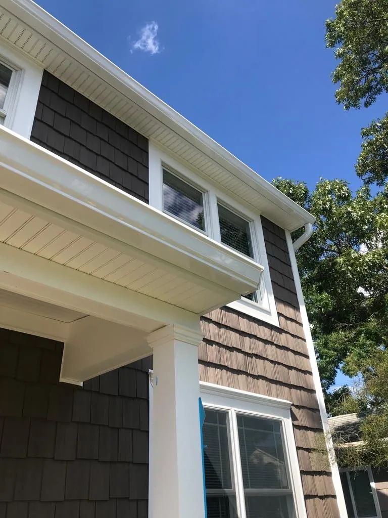 Two-story house exterior with white trim, brown shingle siding, and blue sky overhead