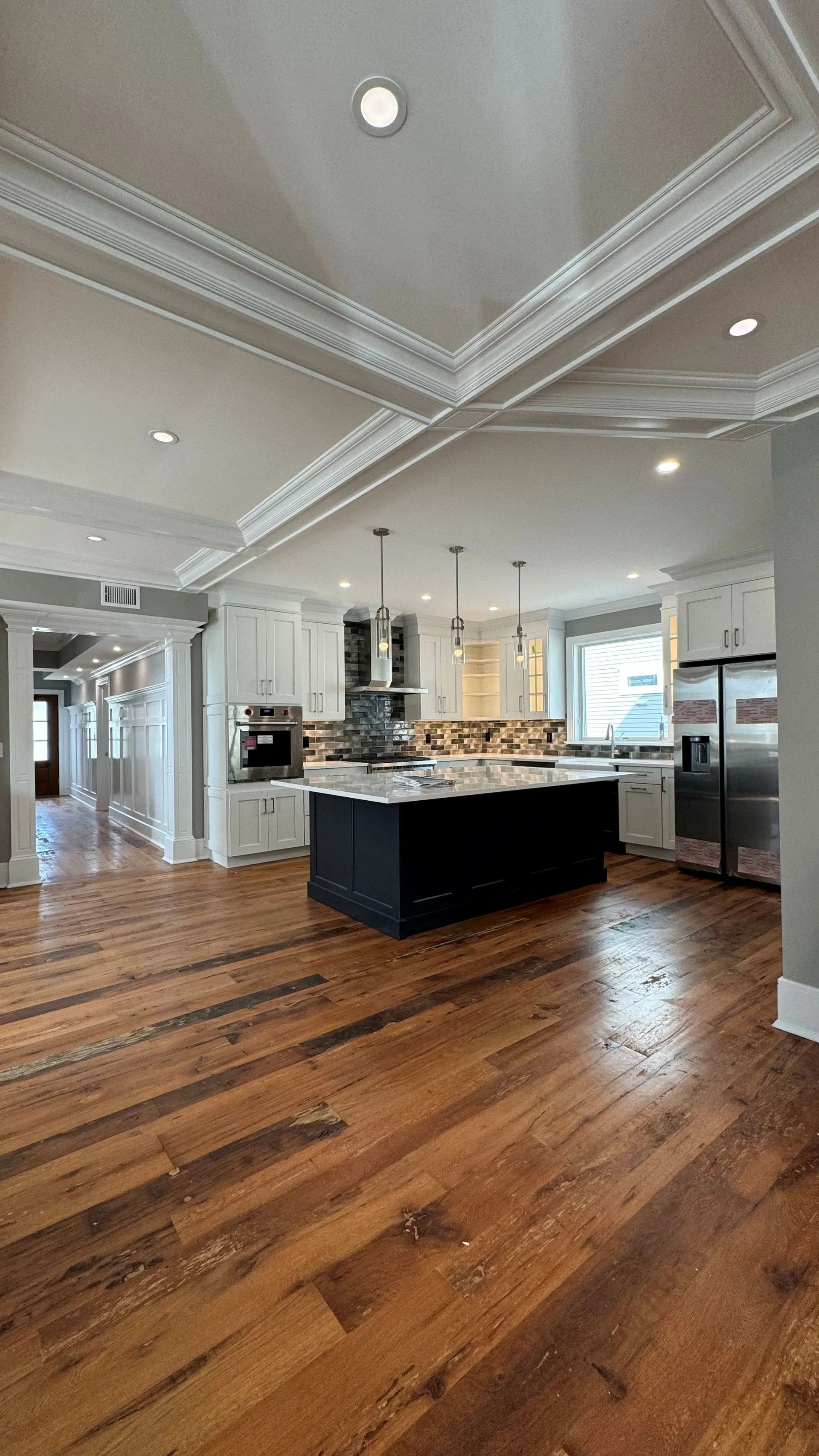 Bright, modern kitchen with a large island, white cabinets, recessed lights, and hardwood floors.