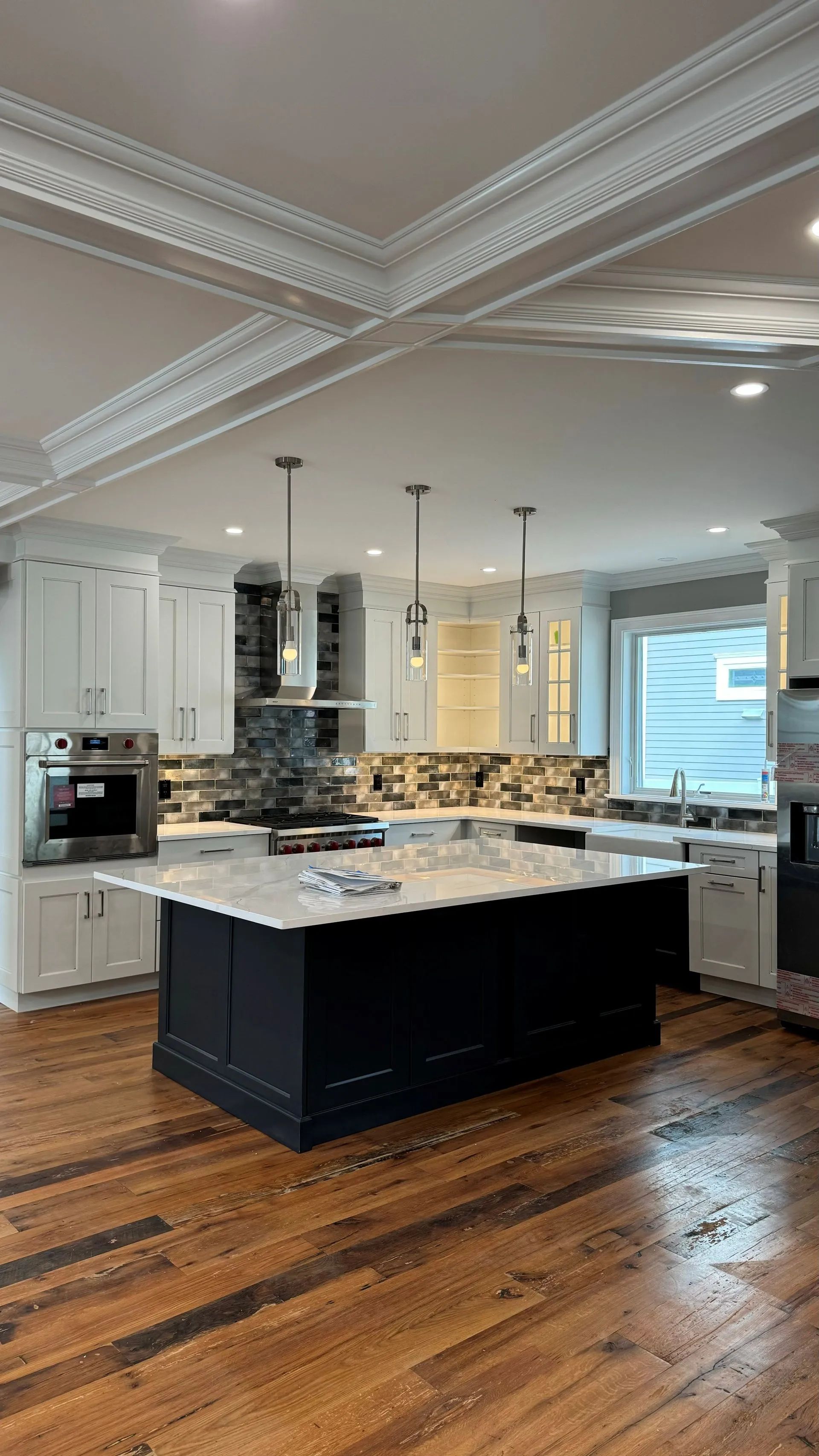 Bright kitchen with white cabinets, black island, granite counters, pendant lights, and hardwood floors.