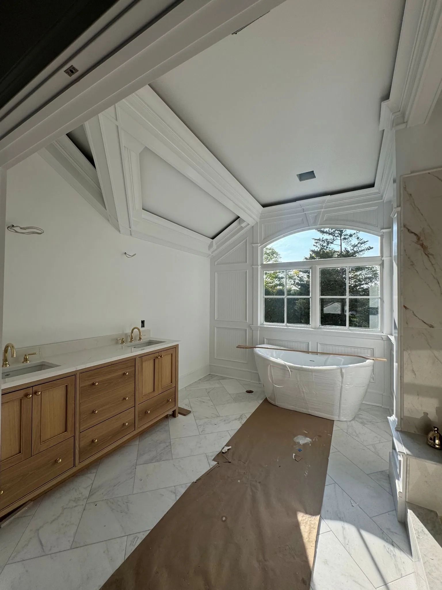 Bright bathroom with vaulted ceiling, wood vanity, freestanding tub, and large window.