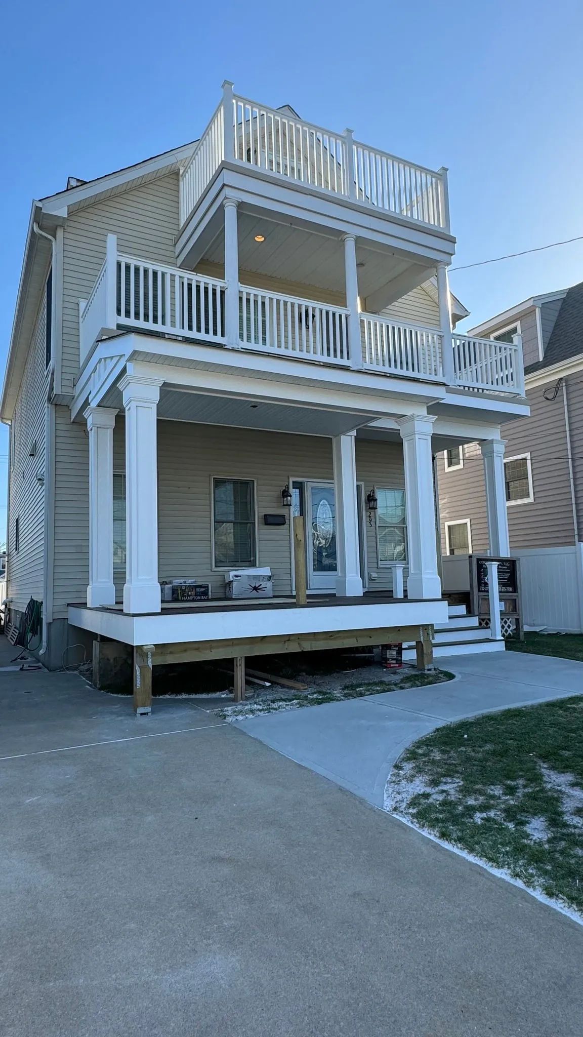 Two-story white house with wraparound porch and rooftop deck, viewed from the driveway.