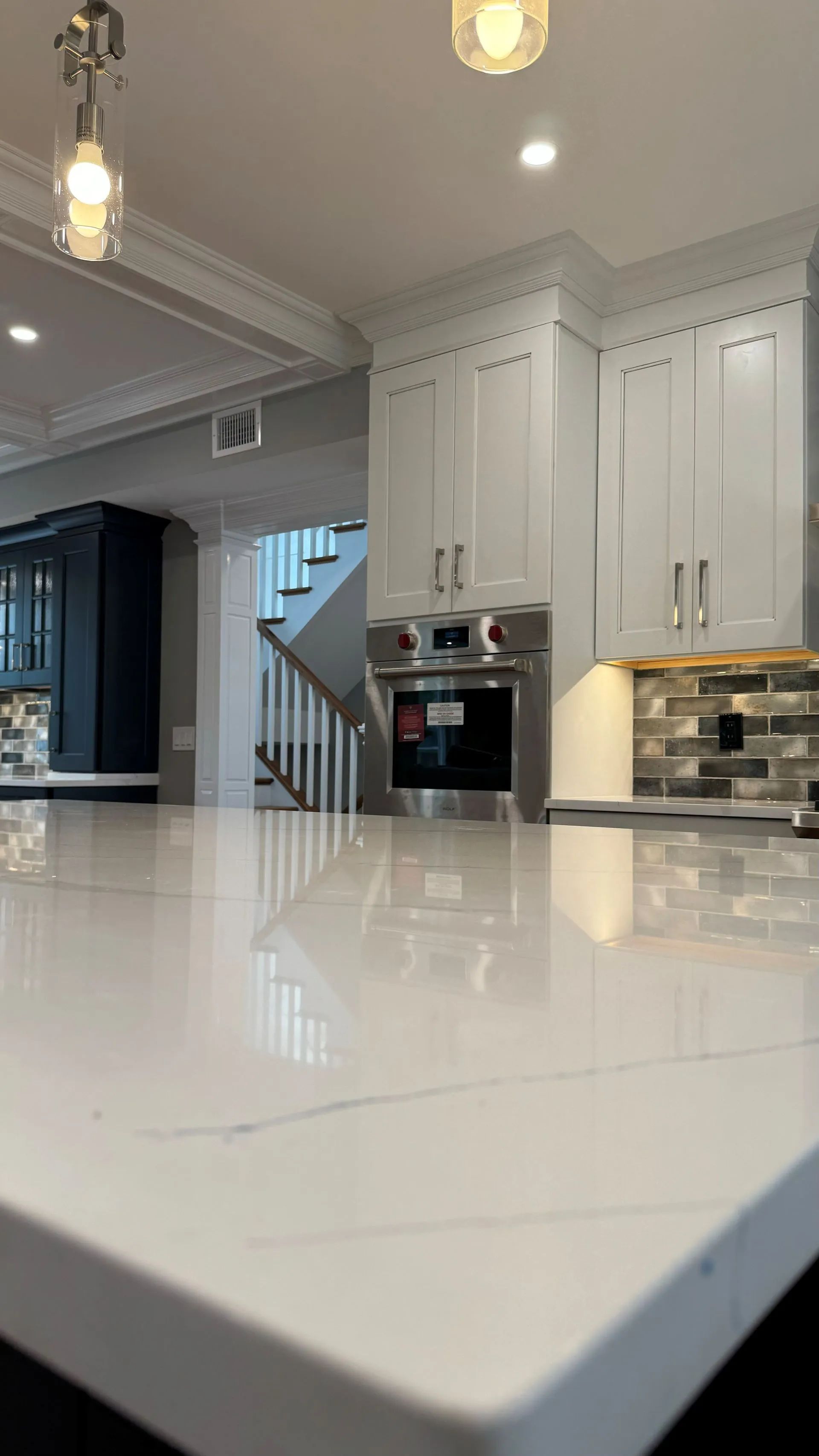 Modern white kitchen with glossy island countertop, cabinets, pendant lights, and built-in oven