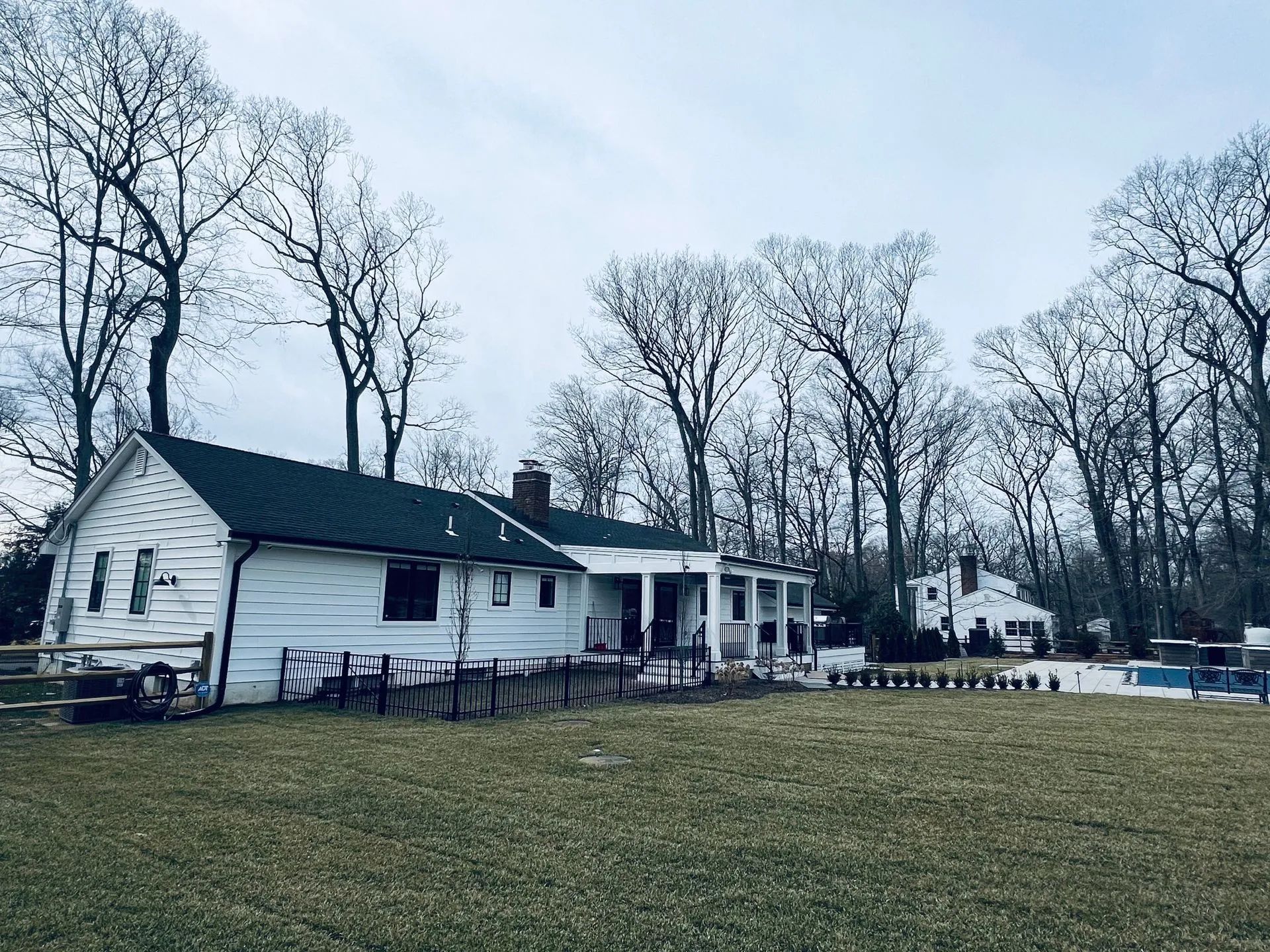 White house with black roof beside a grassy yard and leafless trees on an overcast day