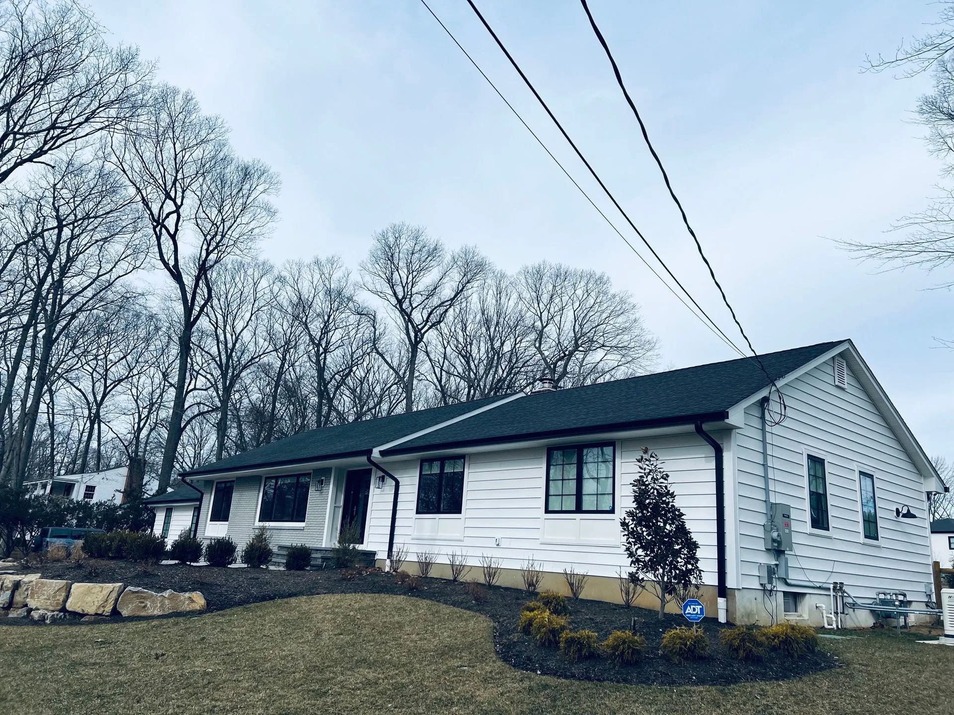 Single-story white house with black roof and trees on a cloudy day
