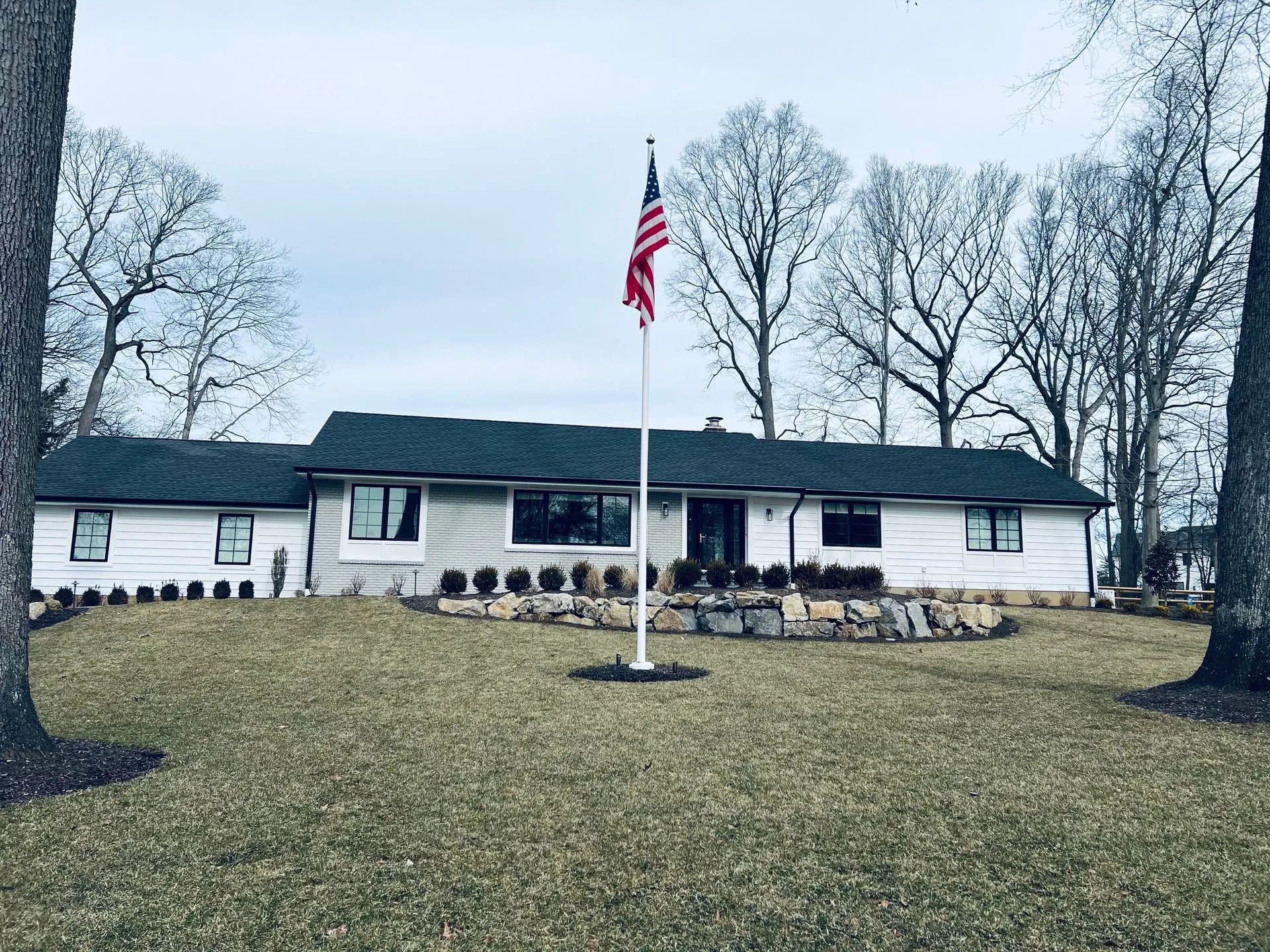 White house with dark roof and American flag on a lawn under cloudy sky