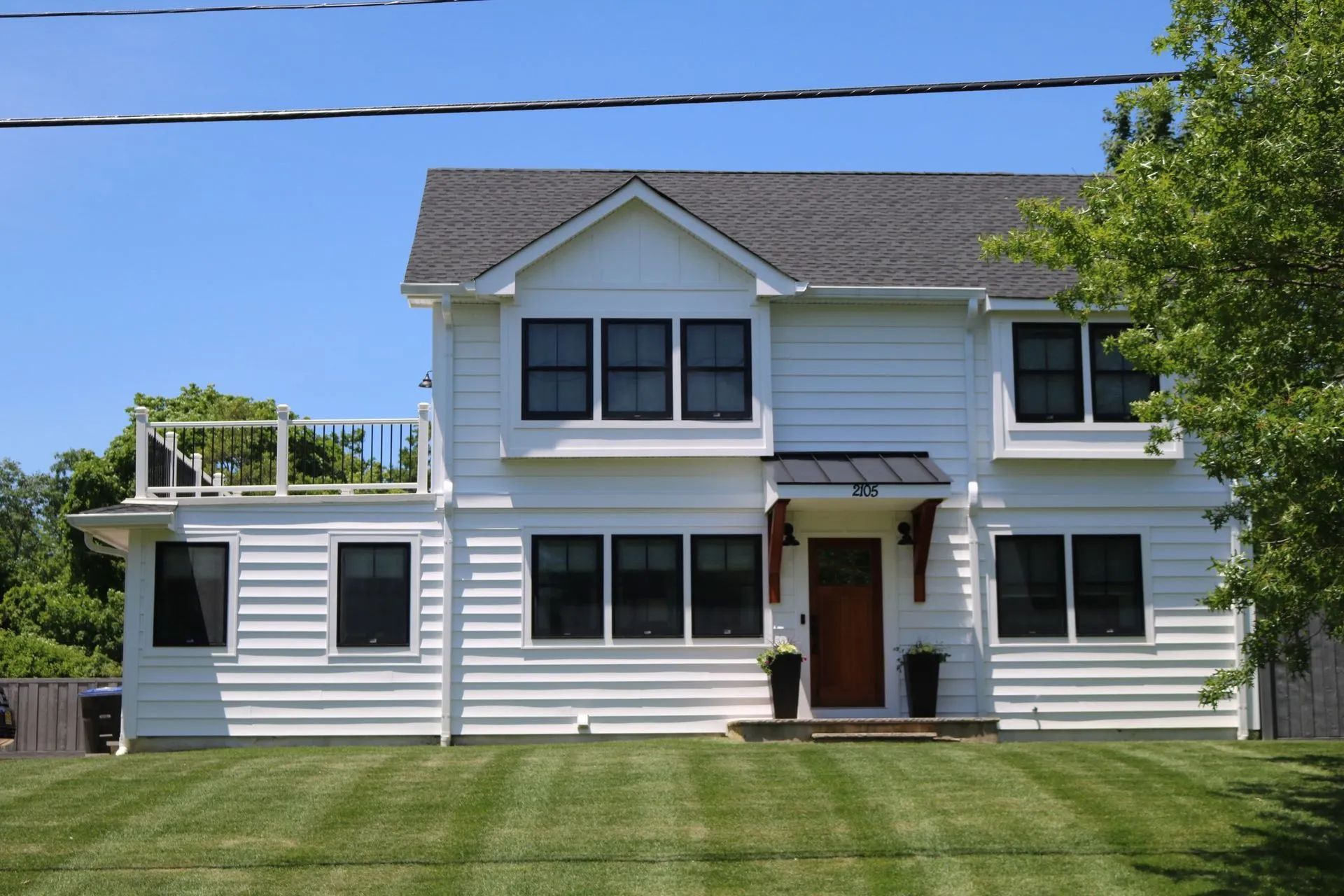 White two-story house with gray siding, dark shutters, front lawn, and a tree on the right side