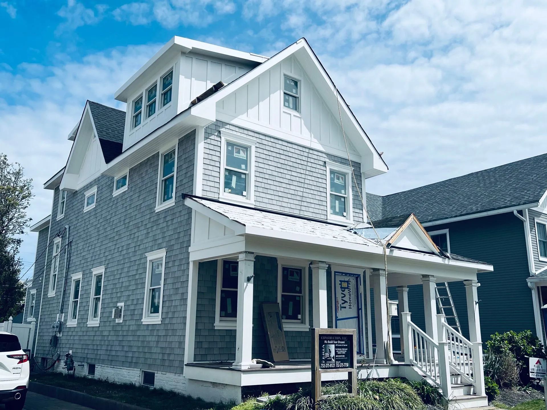 Two-story gray house with white trim and porch under a bright blue sky