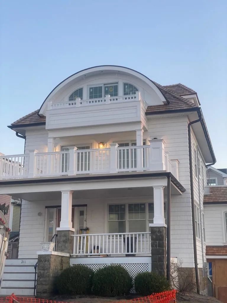 Two-story white house with a balcony, arched upper window, and front porch under a blue sky