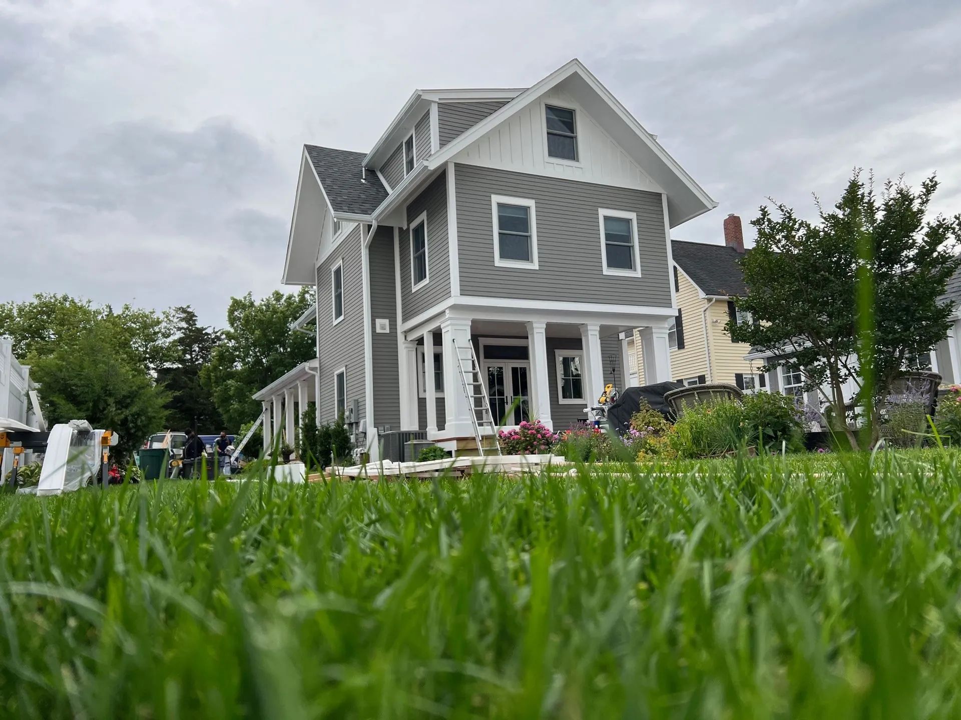 Gray house with white trim and steep roof, viewed from low grassy lawn under a cloudy sky