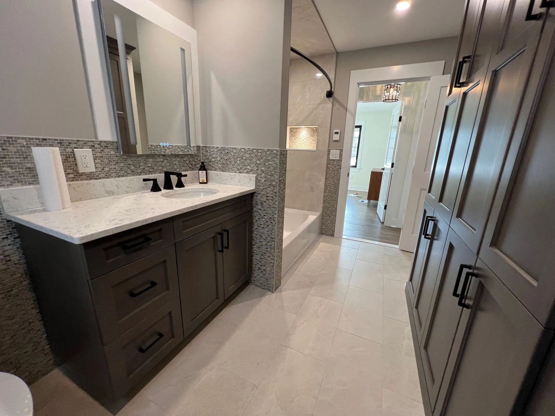 Modern bathroom with dark vanity, white countertop, mirror, and hallway view.