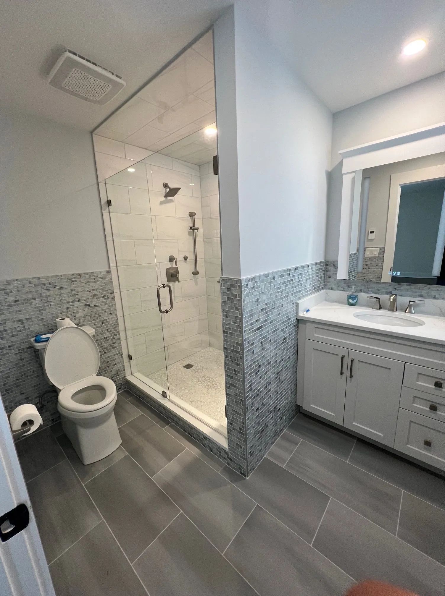 Accessible bathroom with toilet, glass shower, and vanity with sink and mirror.