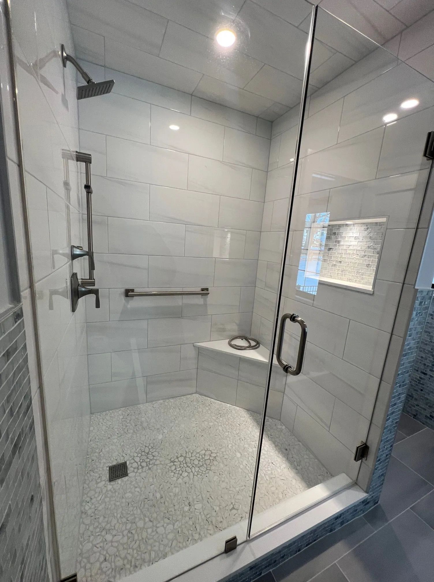 Modern glass walk-in shower with white tile, black fixtures, and a built-in bench.