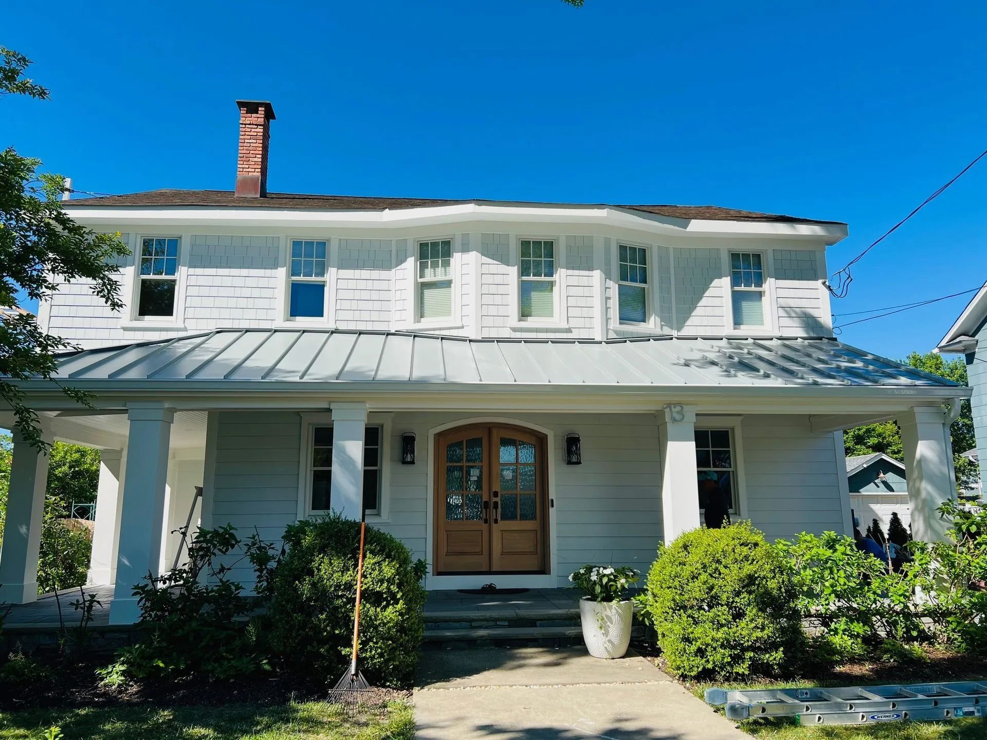 White two-story house with a porch, blue shutters, and a brick chimney under a clear blue sky