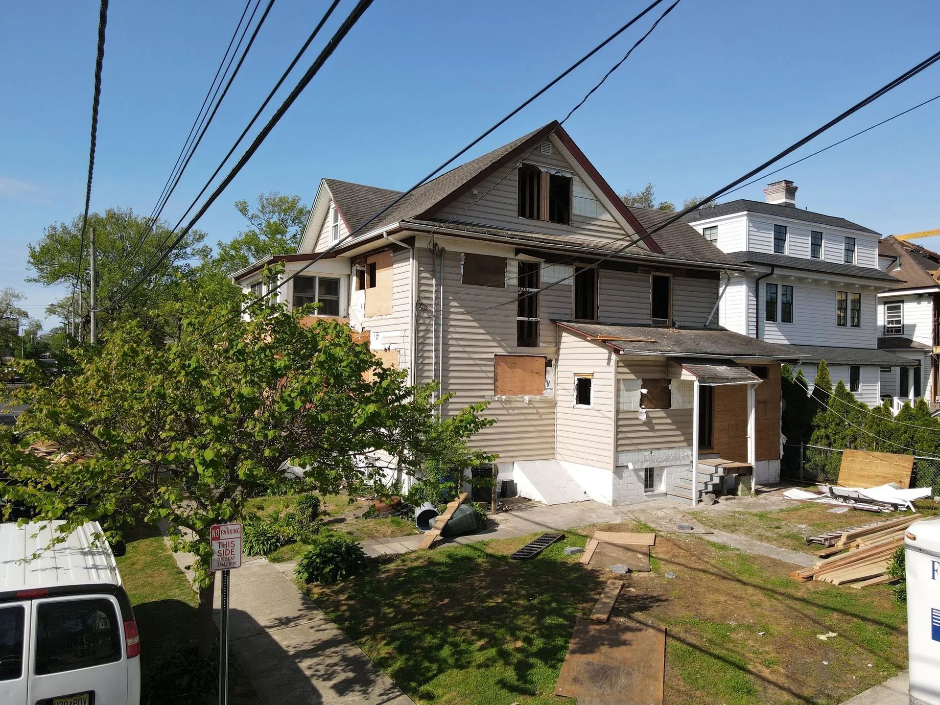 Partially renovated house with white siding and exposed wood, viewed from a grassy yard under blue sky