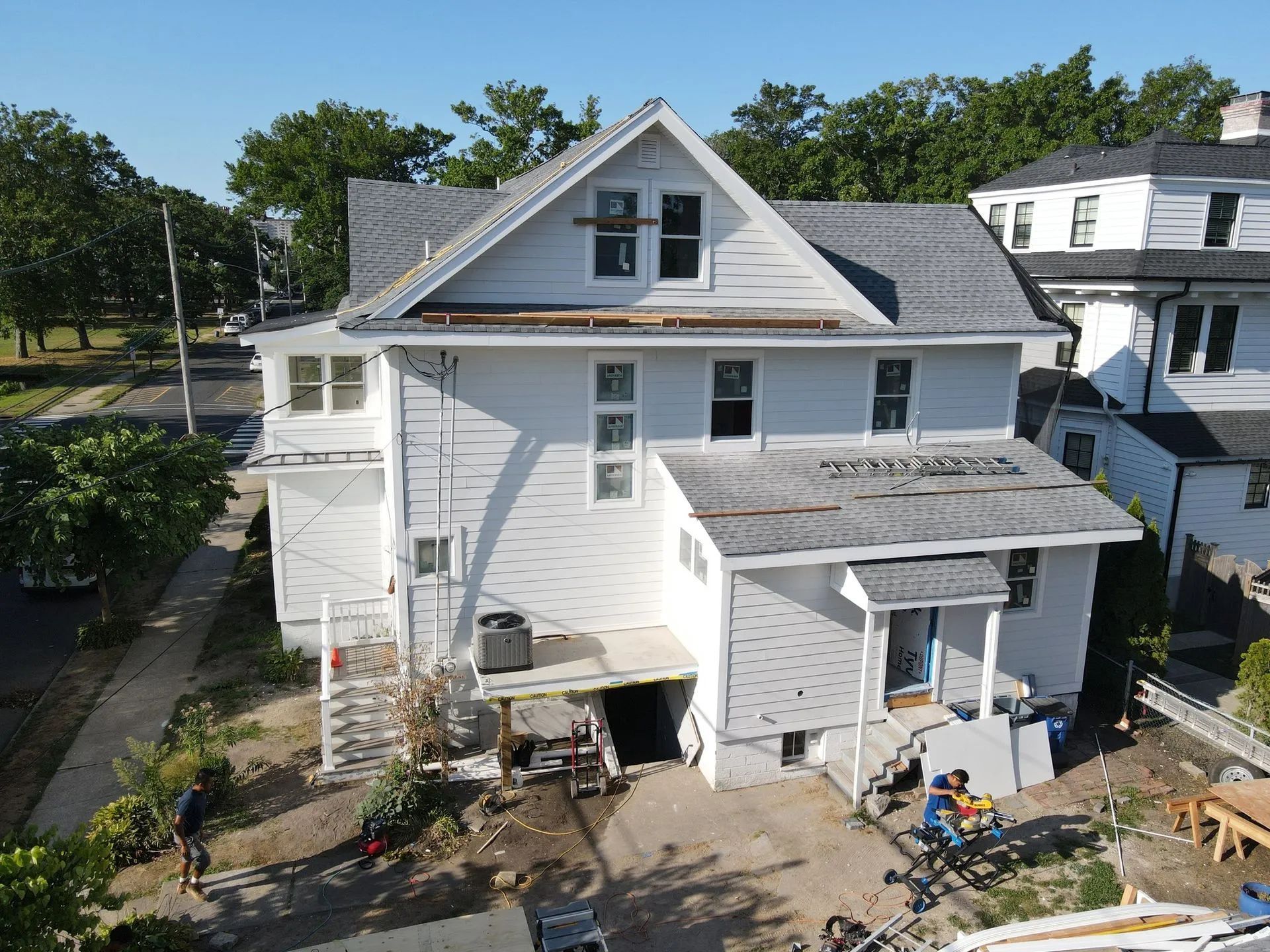 White two-story house under renovation with ladders, tools, and construction materials in front