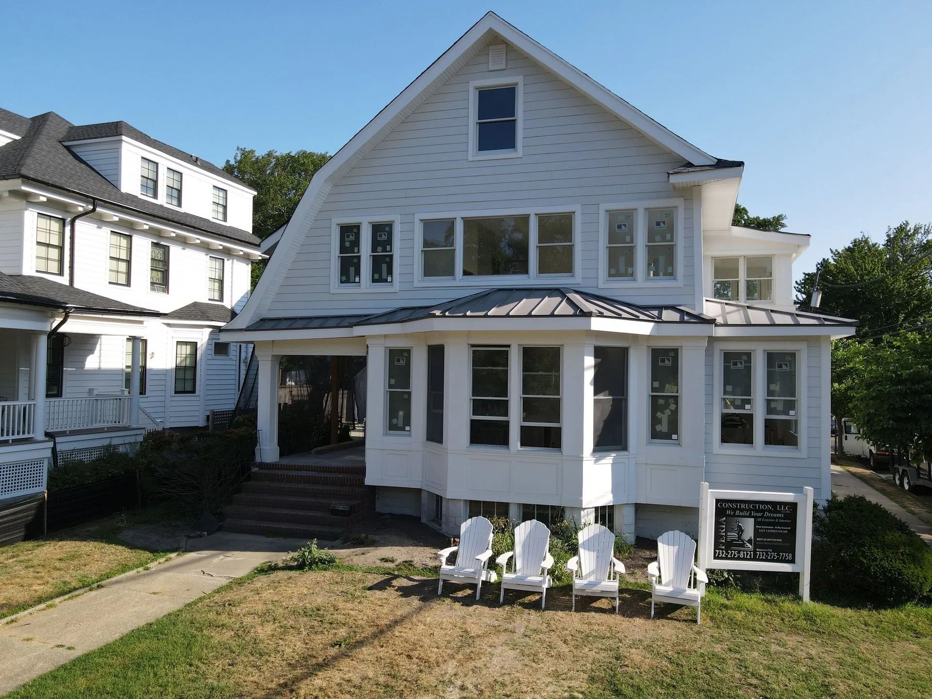 White two-story house with a porch, front lawn, and white chairs outside