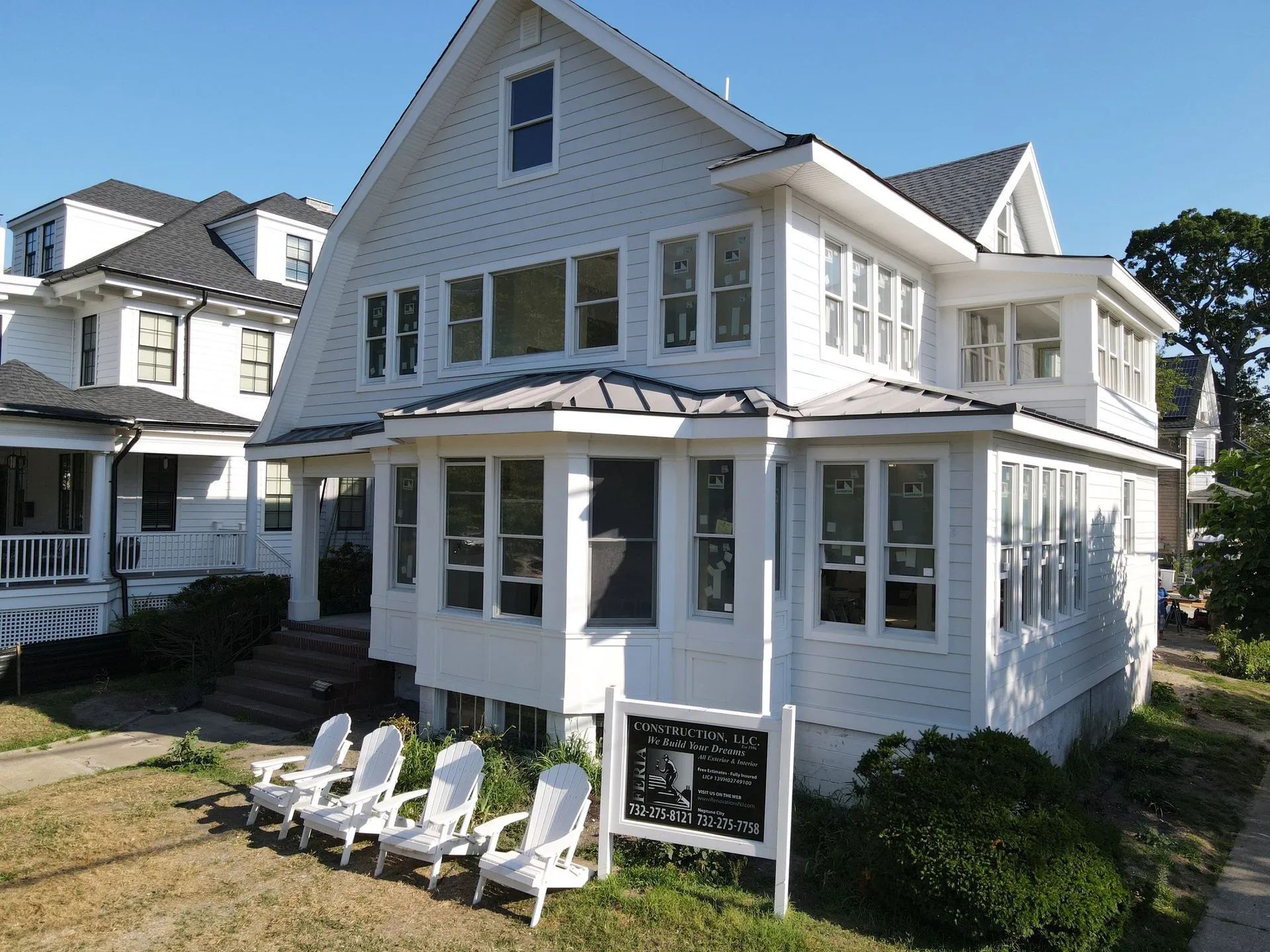 White seaside house with wraparound porch, dormer windows, and Adirondack chairs on the lawn