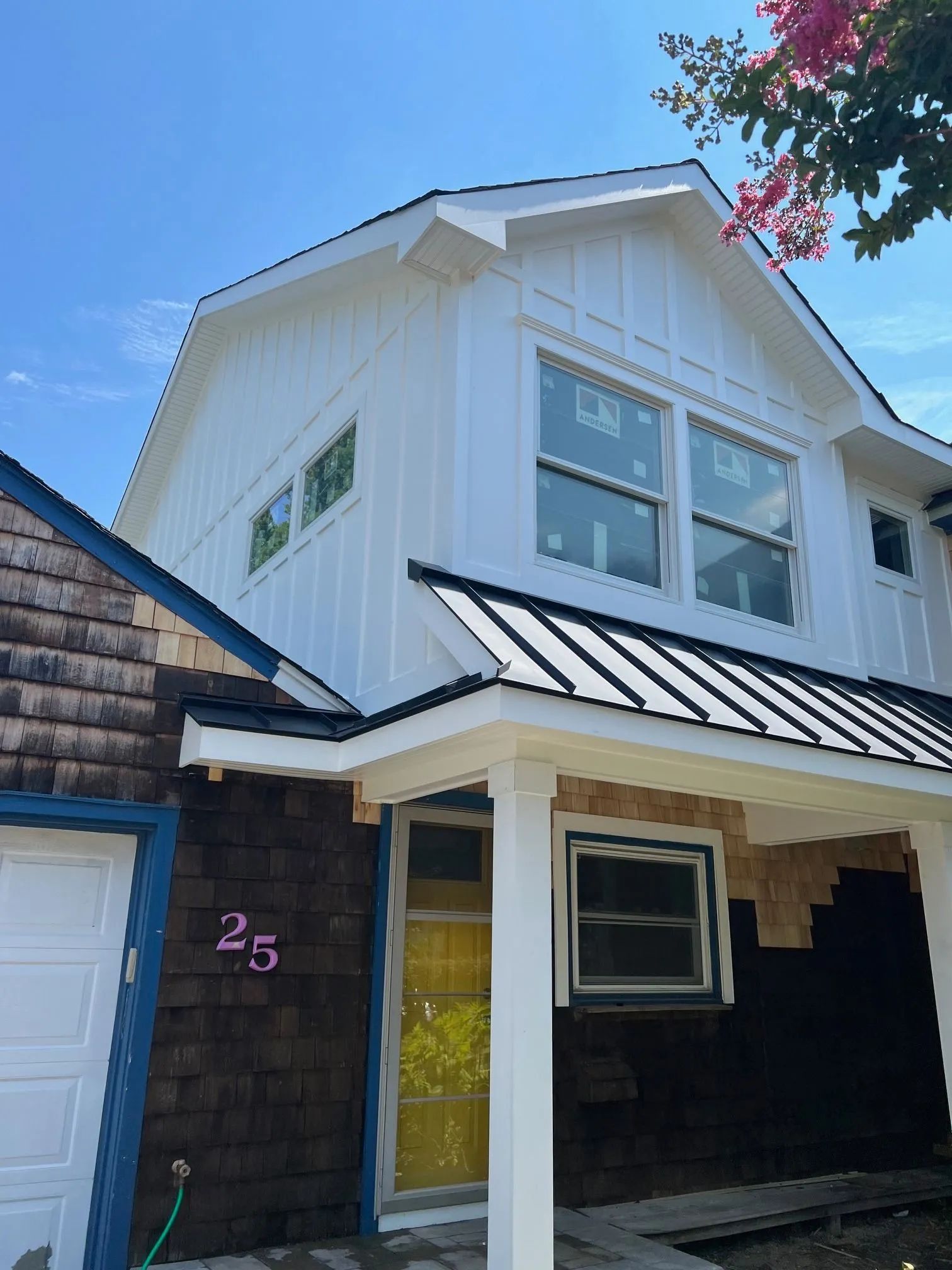 White two-story house with black porch, garage, and pink house number 25 under a blue sky