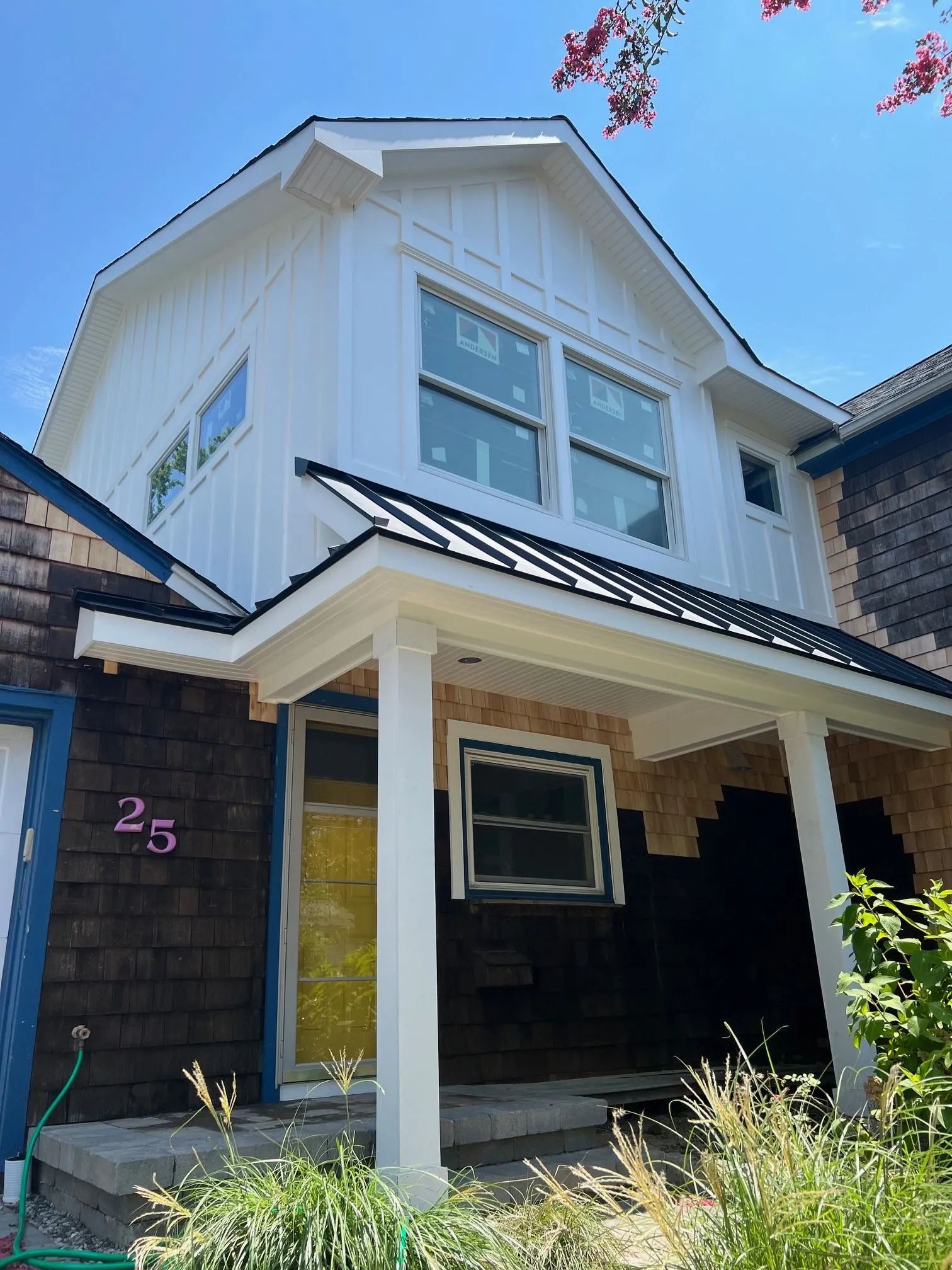 White two-story house with dark trim, front porch, and visible house number 25 under a blue sky