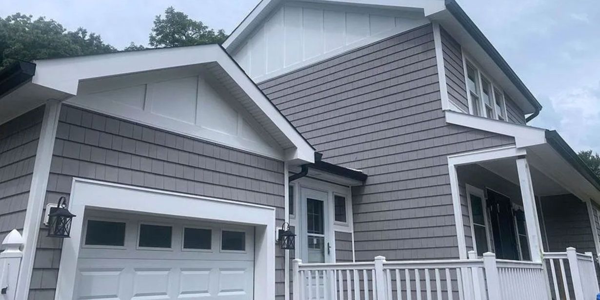Gray house exterior with attached garage, white trim, and front porch under a cloudy sky