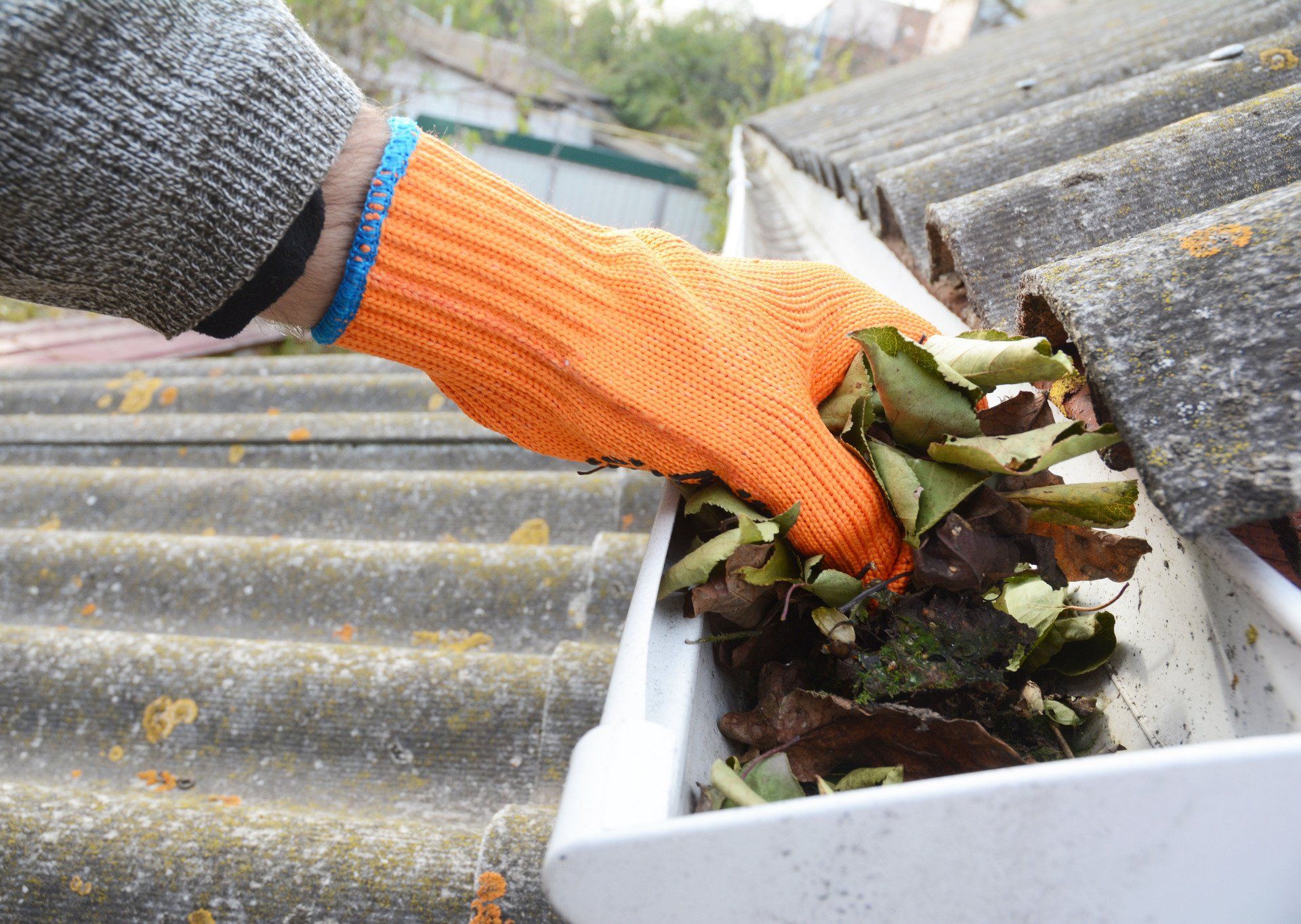 A person wearing orange gloves is cleaning a gutter with leaves.