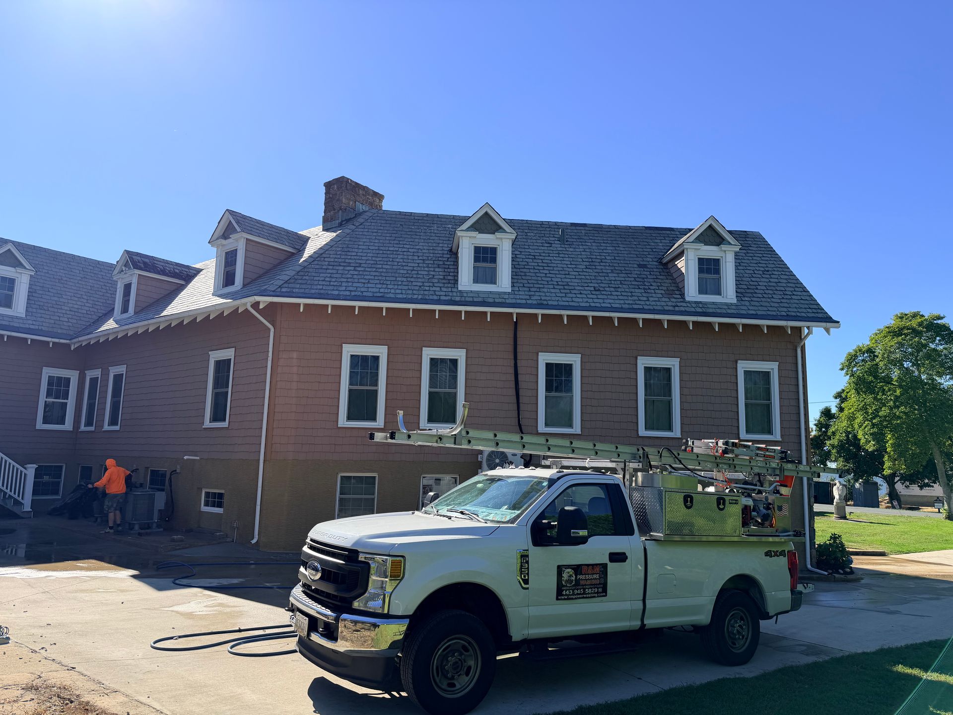 White work truck parked in front of a two-story brown building with workers visible. Sunny day.