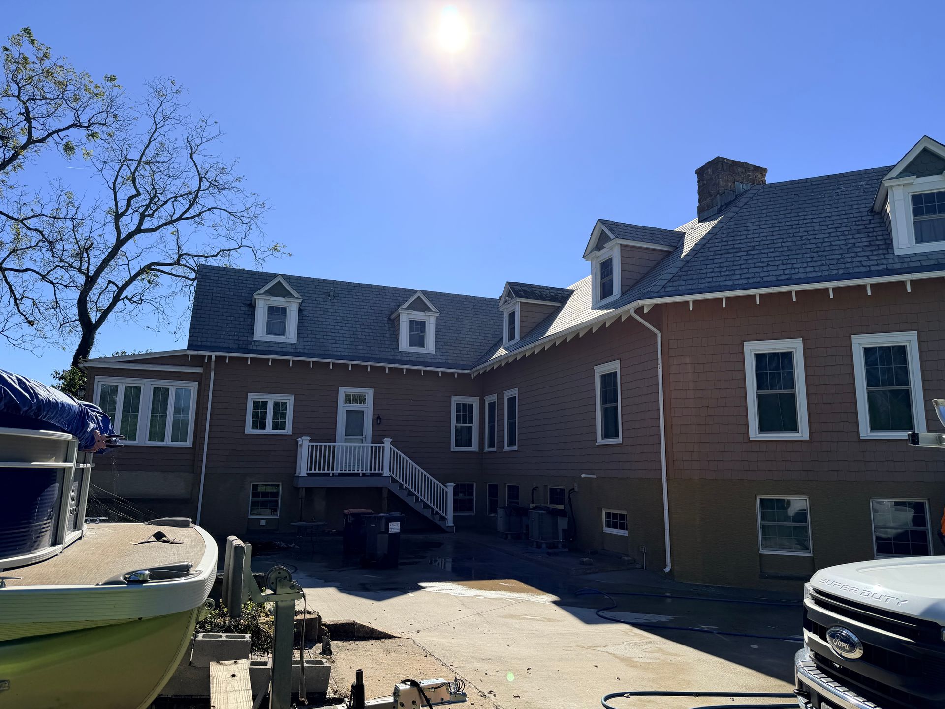 Brown building with multiple dormer windows on a sunny day. Boat and truck in the foreground.